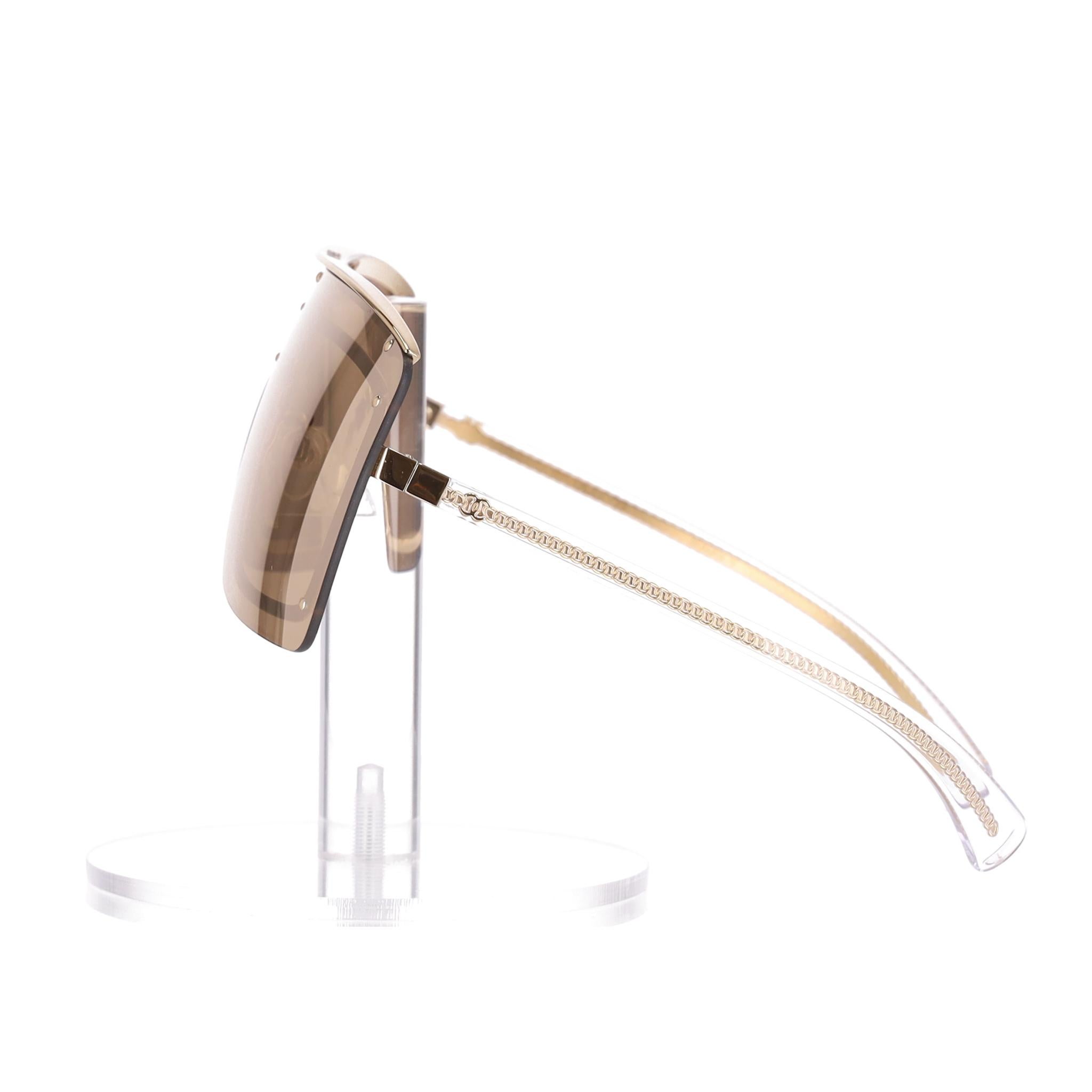 We Adore - Lunettes de soleil miroirs Chanel Shield avec chaîne et logo 'CC' sur les branches

Lunettes de soleil dorées en forme de masque, dotées de verres enveloppants, de clous dorés sur le devant et d'une barre supérieure en métal gravée