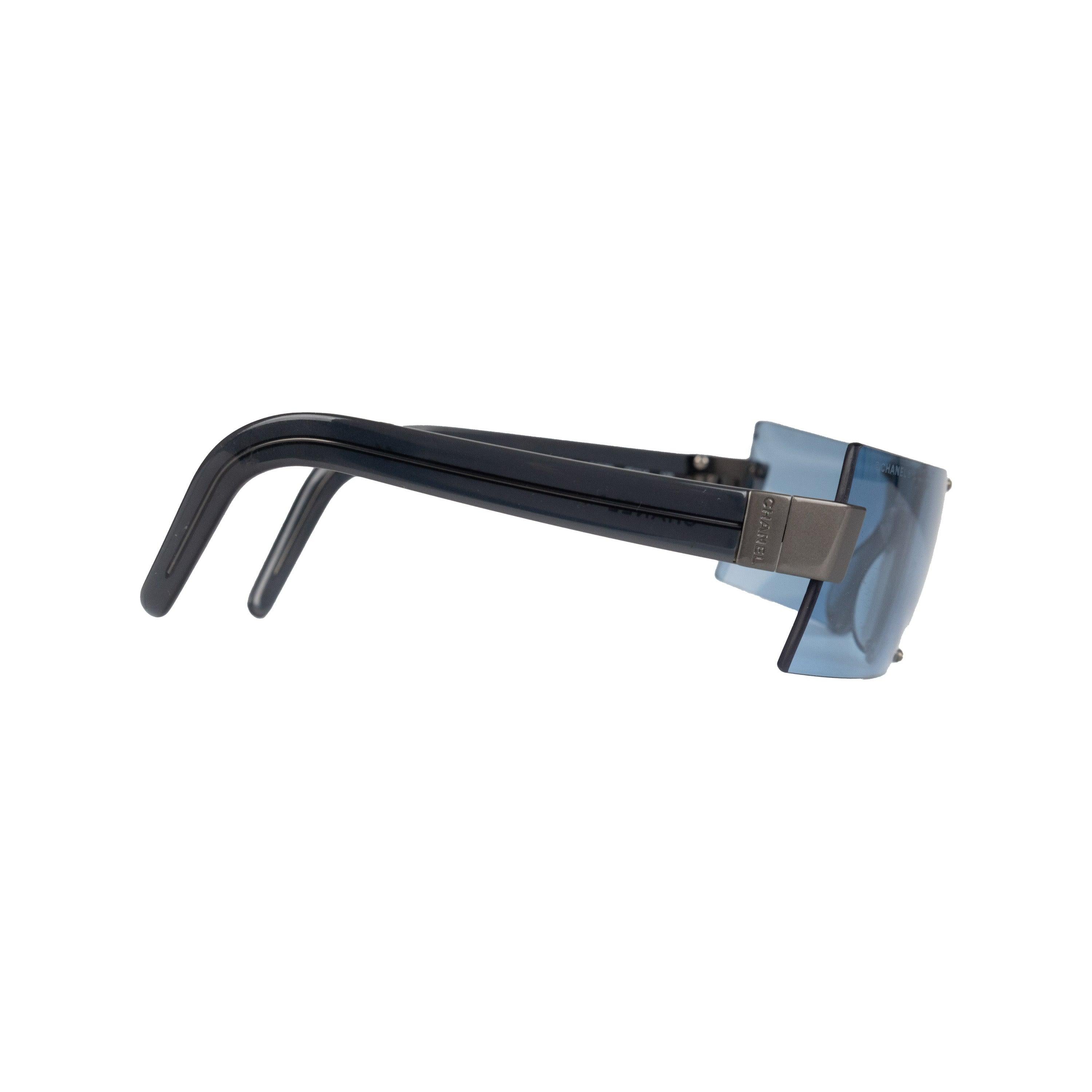 Introducing the Chanel Shield Sunglasses from the 00s collection. These visor-style sunglasses feature a rectangular silhouette and rimless mirrored lenses for a sleek and modern look. Made with blue lenses and grey metal hardware, these sunglasses