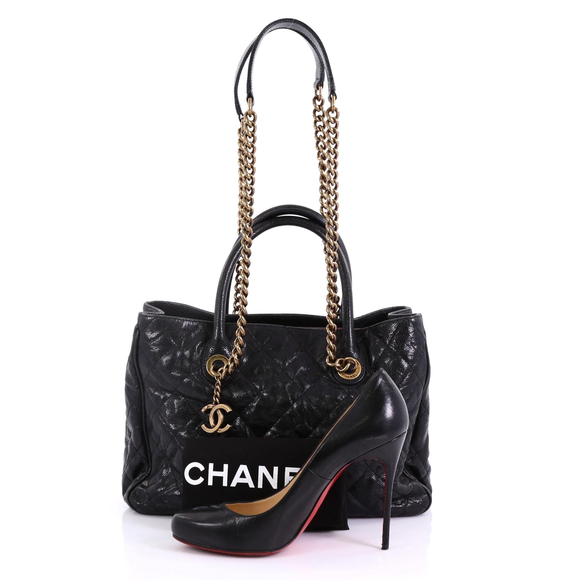 This Chanel Shiva Tote Quilted Caviar Medium, crafted from black quilted caviar leather, features dual rolled leather handles, chain link straps with shoulder pads, and aged gold-tone hardware. It opens to a burgundy fabric interior with middle zip