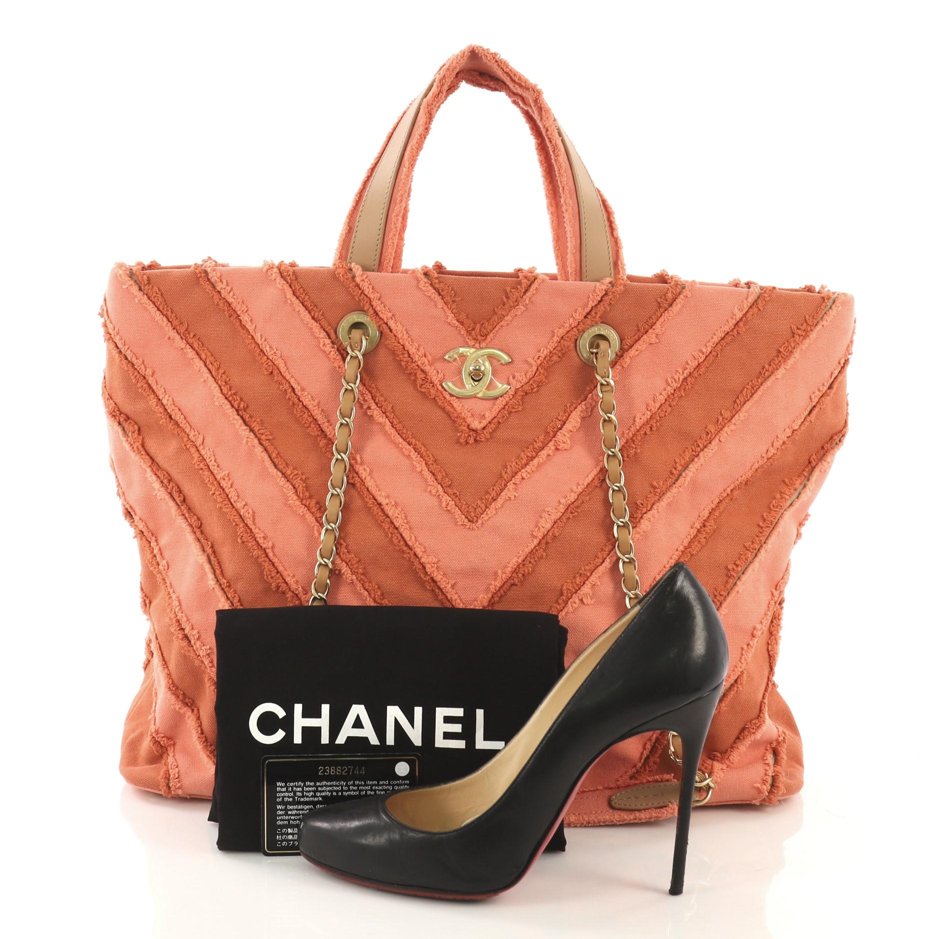 This Chanel Shopping Tote Chevron Canvas Patchwork Large, crafted from pink chevron canvas patchwork, features dual top handles, woven-in leather chain straps with shoulder pads, protective base studs and matte gold-tone hardware. Its CC turn-lock