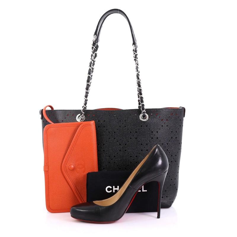 This Chanel Shopping Tote Perforated Caviar Small, crafted in black perforated caviar leather, features woven-in leather chain straps with leather pads and silver-tone hardware. It opens to an orange microfiber interior. Hologram sticker reads: