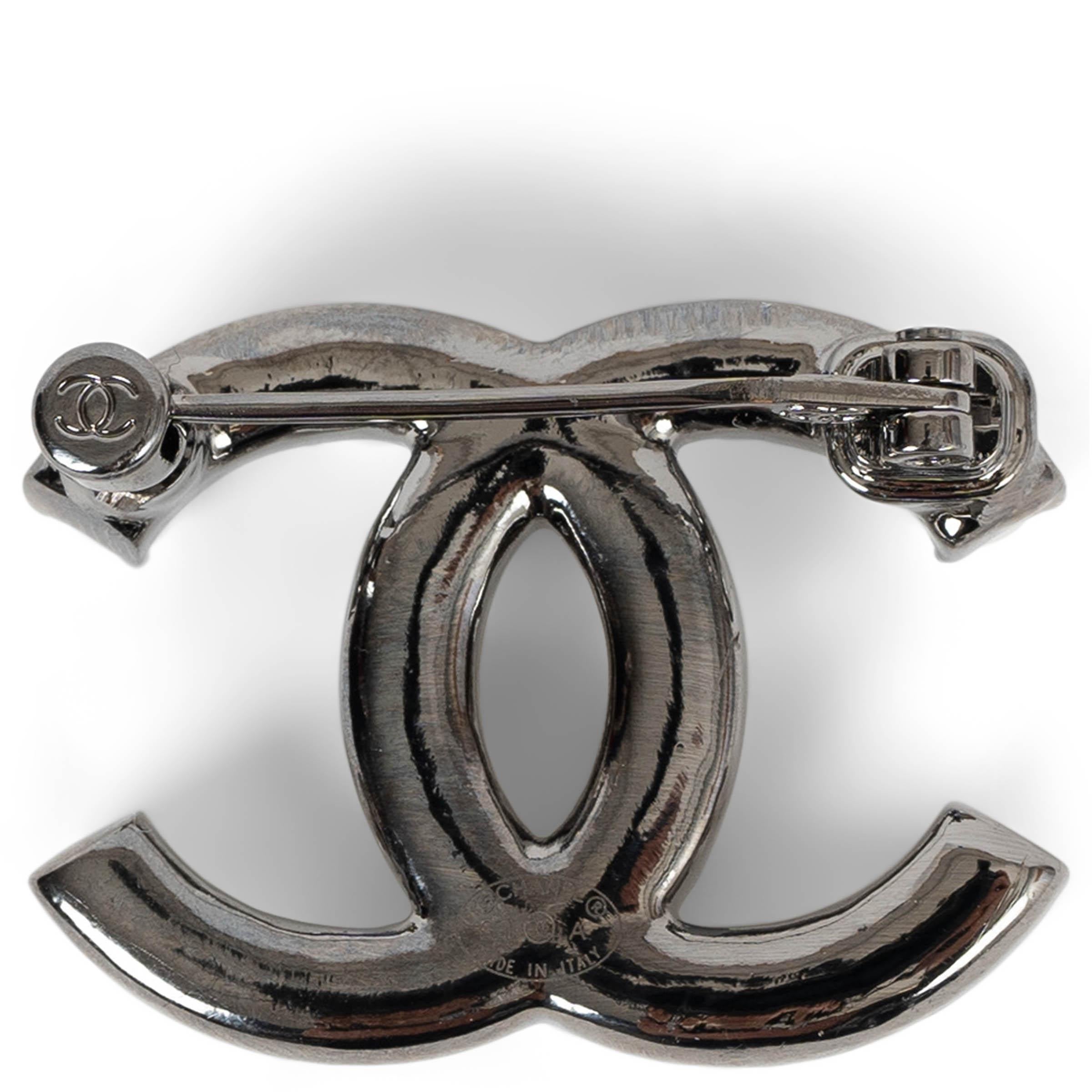 This 100% authentic Chanel CC brooch in dark silver-tone metal is an elegant statement piece, adorned with large pearly white resin cabochon pearls and shimmering small crystals. The contrast of luminous pearls and delicate sparkle enhances its
