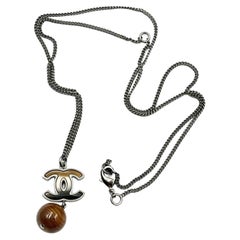 Chanel, collier pendentif CC en bois pétrifié argenté 