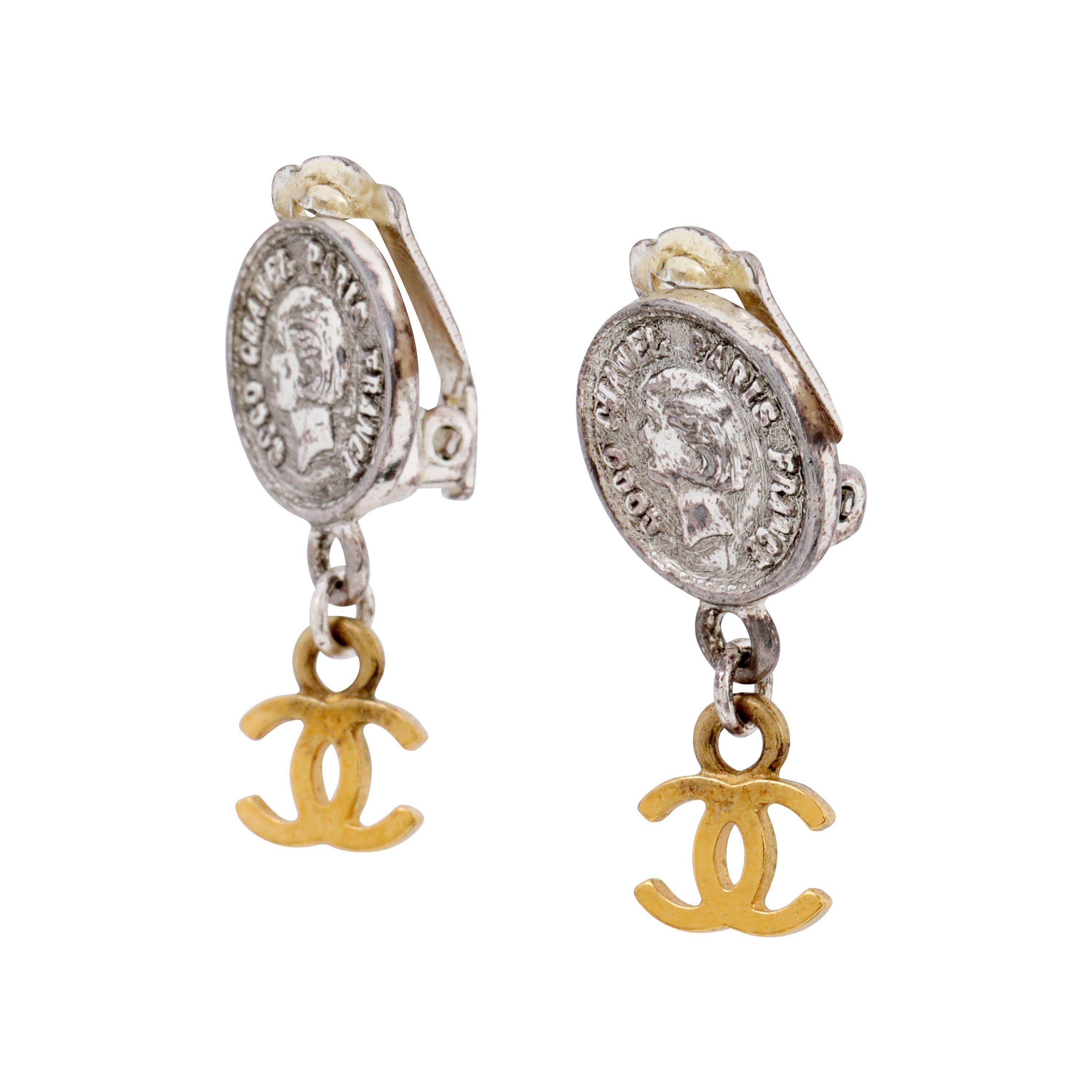 These authentic Chanel Silver Coco Coin Dangle Earrings are in excellent condition from the Spring 1997 Collection.  Silver “coins” featuring Coco in profile with clip on backs.  Gold tone interlocking CC dangles delicately.    Made in France. Pouch
