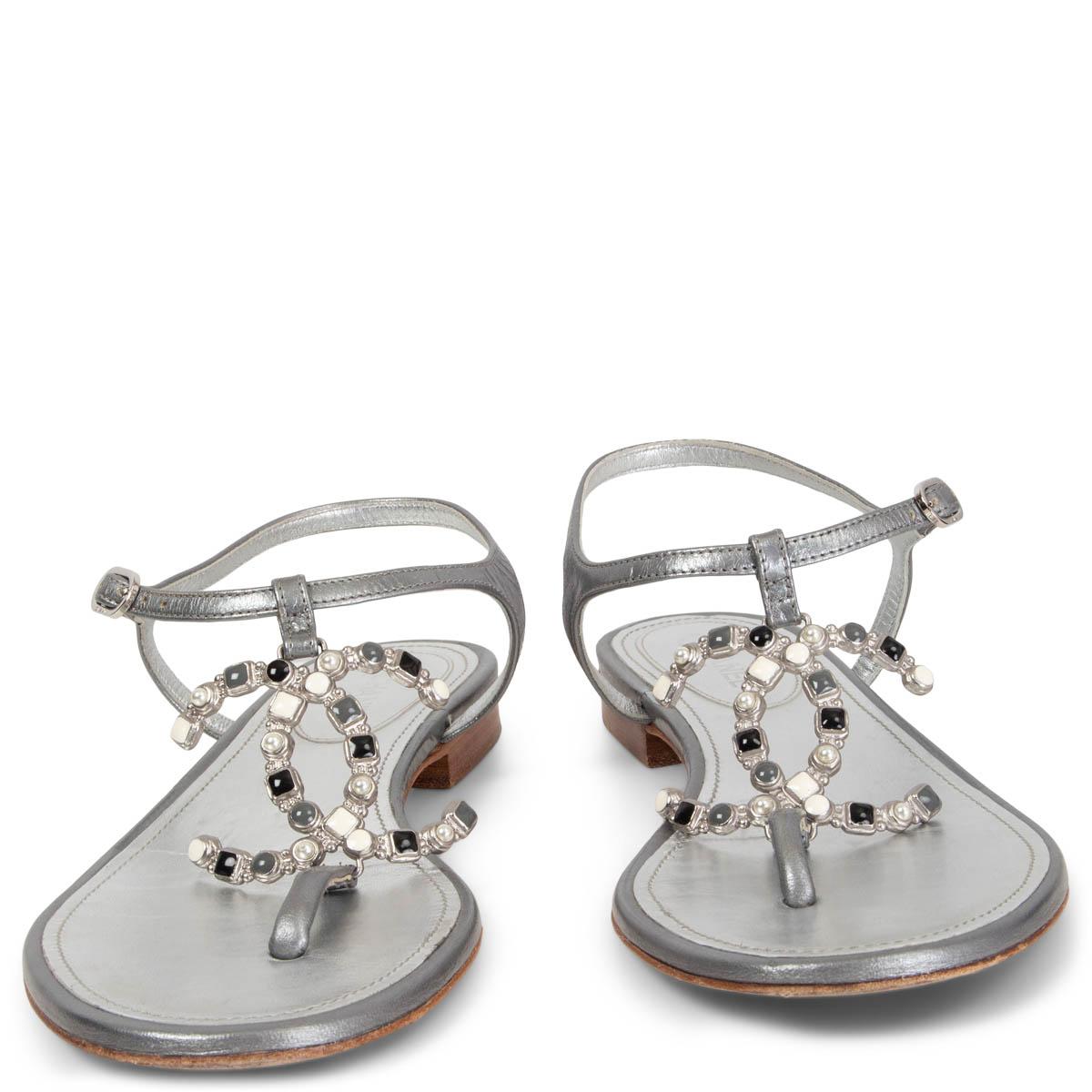 100% authentic Chanel 2019 Stone Embellished CC Flat T-Strap Sandals in metallic silver leather featuring black, white and grey stone and pearl embellished CC buckle. Have been worn and are in excellent condition.