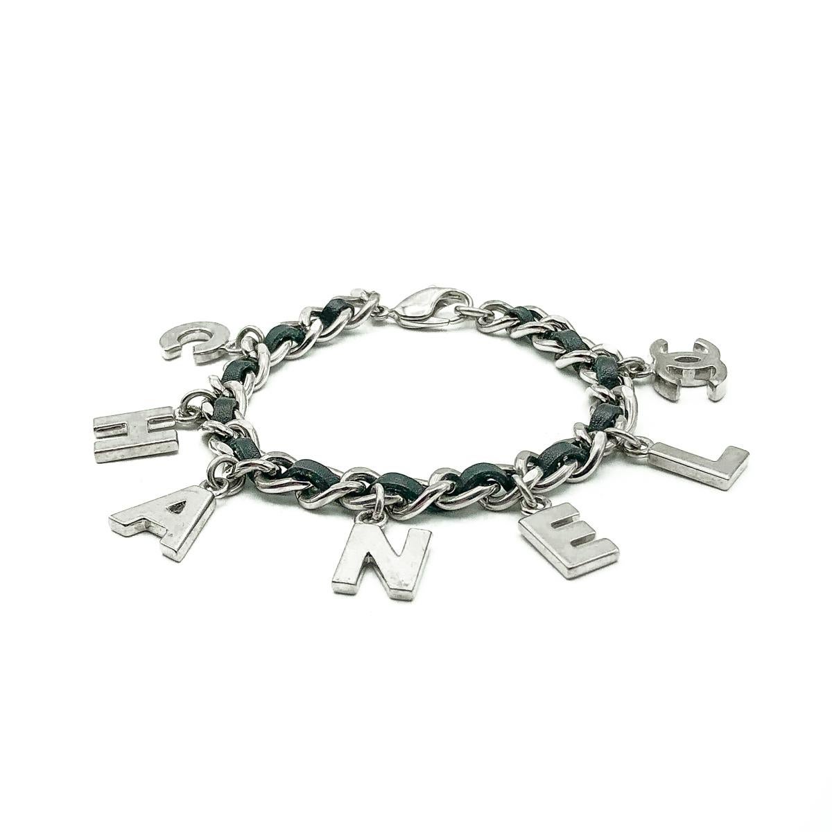 An ultra cool Chanel Letter Charm Bracelet from 2004. Crafted in rhodium plated metal and leather. Featuring a chunky flattened curb link chain threaded with soft black leather. The letter charms spelling out C H A N E L alongside the iconic