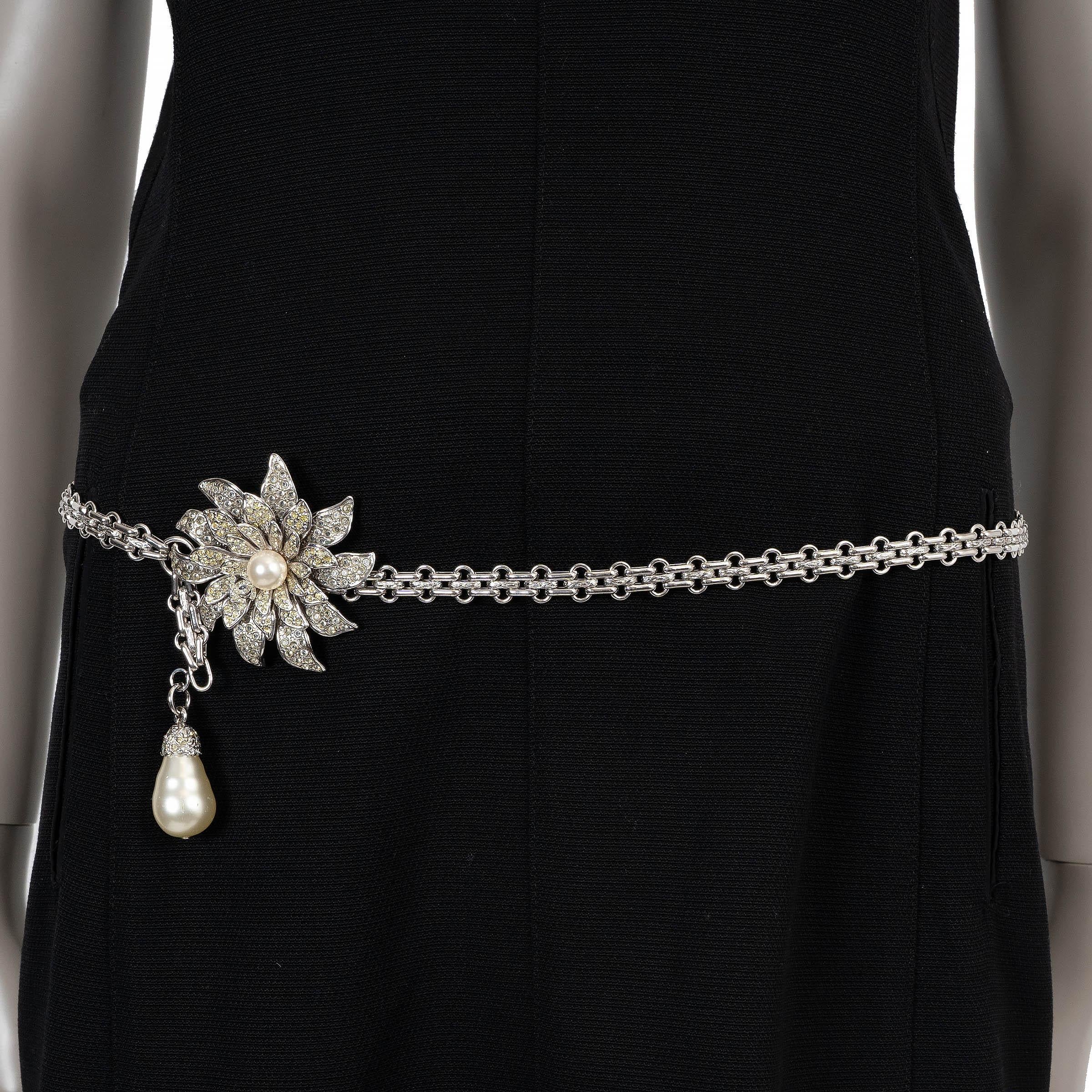 Cette ceinture à mailles en métal argenté 100% authentique de Chanel présente un motif floral saisissant, incrusté de strass clairs et jaunes et rehaussé d'une fausse perle centrale. Une fausse perle pendante en forme de poire ajoute une touche