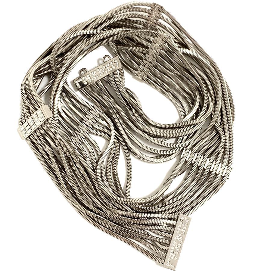 Très belle ceinture CHANEL composée de 8 chaînes en maille serpent en métal argenté. Ces mailles sont maintenues par des pièces métalliques argentées serties de strass baguette et d'inscriptions en strass CHANEL. Le fermoir est un crochet
