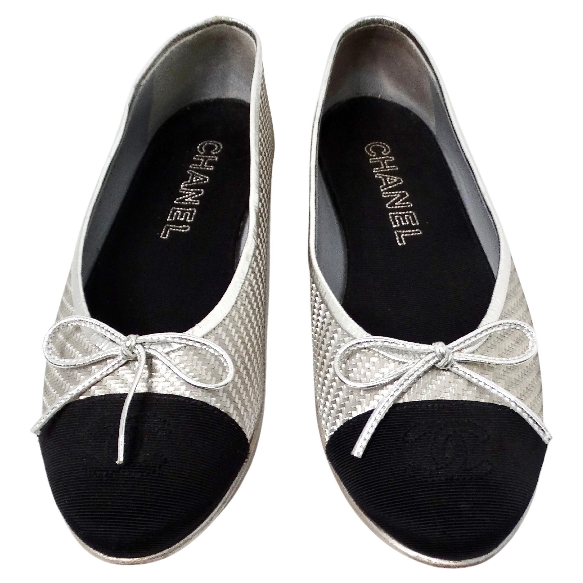 The Chanel Silver Metallic PVC Woven Grosgrain Black Cap Toe Ballet Flats are a stunning example of luxury footwear that seamlessly combines elegance with modern design. Crafted from shimmering silver metallic PVC, these flats exude a sophisticated
