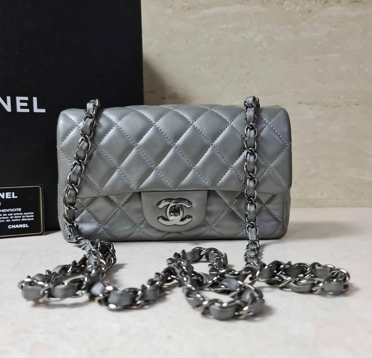 This authentic CHANEL Metallic Lambskin Quilted Mini Rectangular Flap Silver bag features a polished silver chain link shoulder strap threaded with leather, a rear pocket and a front polished silver Chanel CC turn lock. 
This opens to a matching