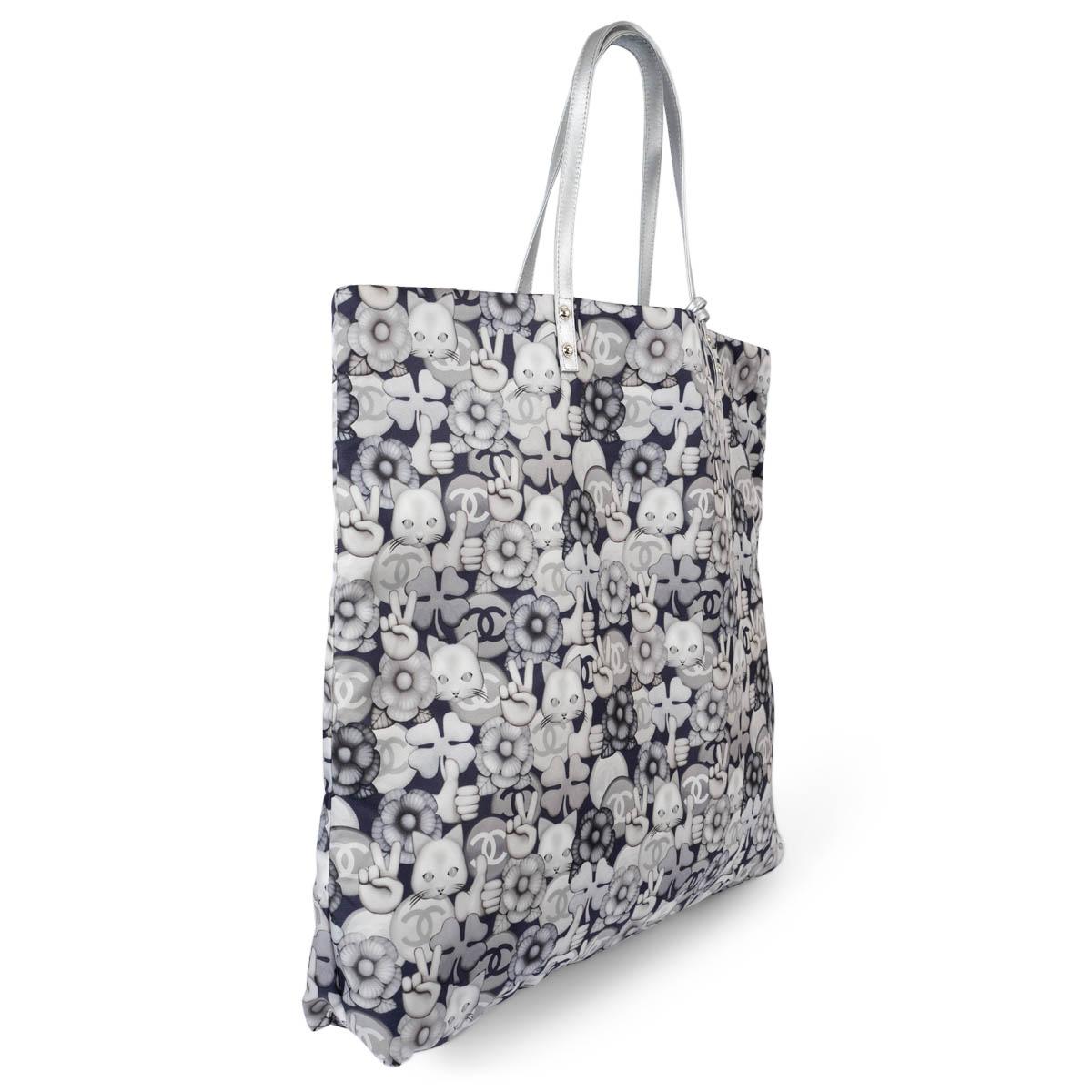 100% authentic Chanel Emoticon Large Shopping tote in navy blue and silver printed nylon. Features metallic silver leather handles and zip pouch. Lined in quilted navy blue nylon with an open pocket against the back. Has been carried once and is in
