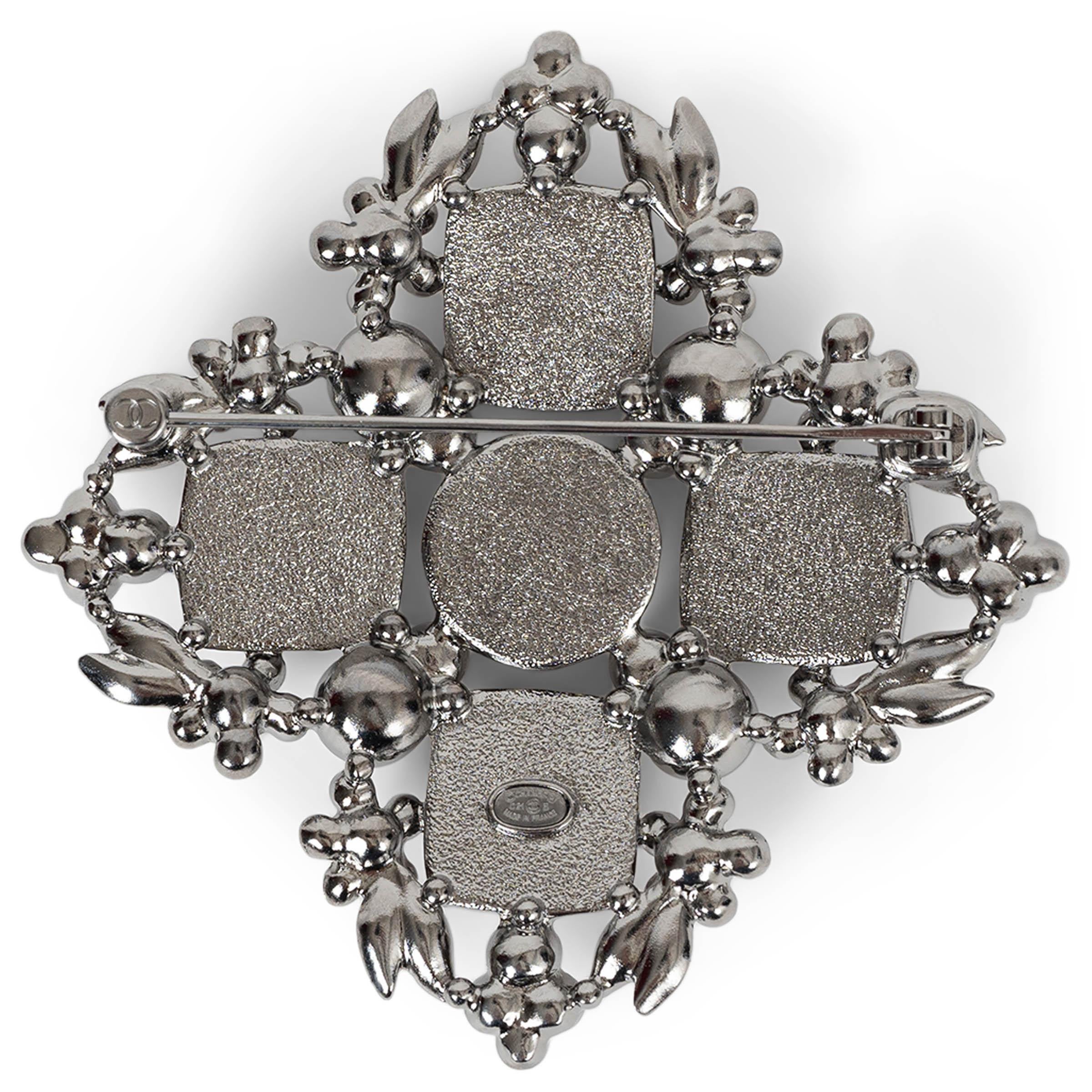 This 100% authentic Chanel brooch in silver-tone metal is a dazzling statement piece, fully encrusted with shimmering strass and luminous pearly white resin pearls. Four large pink stones add a striking contrast, enhancing its elegant design. A