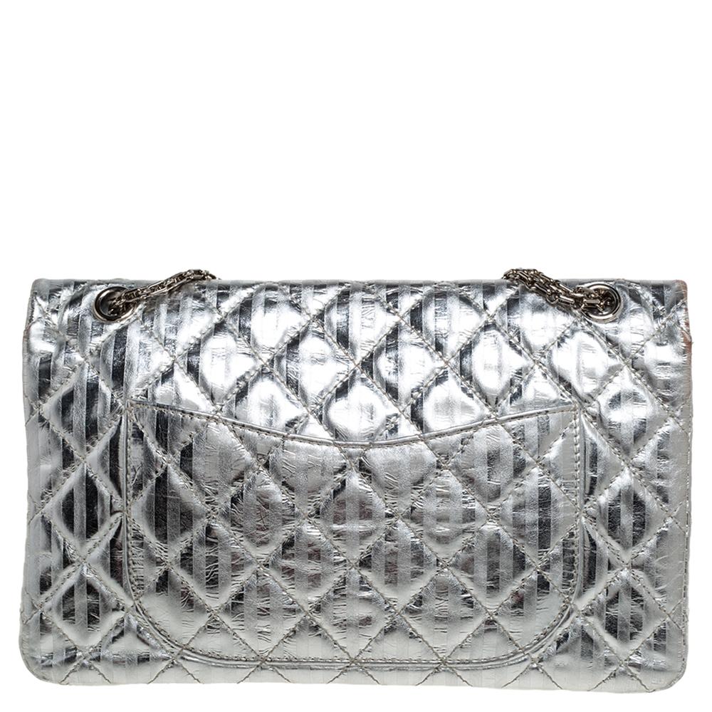 Le borse con patta di Chanel sono iconiche e degne di nota nella storia della moda. Qui abbiamo una grande Reissue 2.55. Realizzata in pelle argentata, presenta strisce e il caratteristico motivo a trapunta, oltre all'iconico lucchetto Mademoiselle.