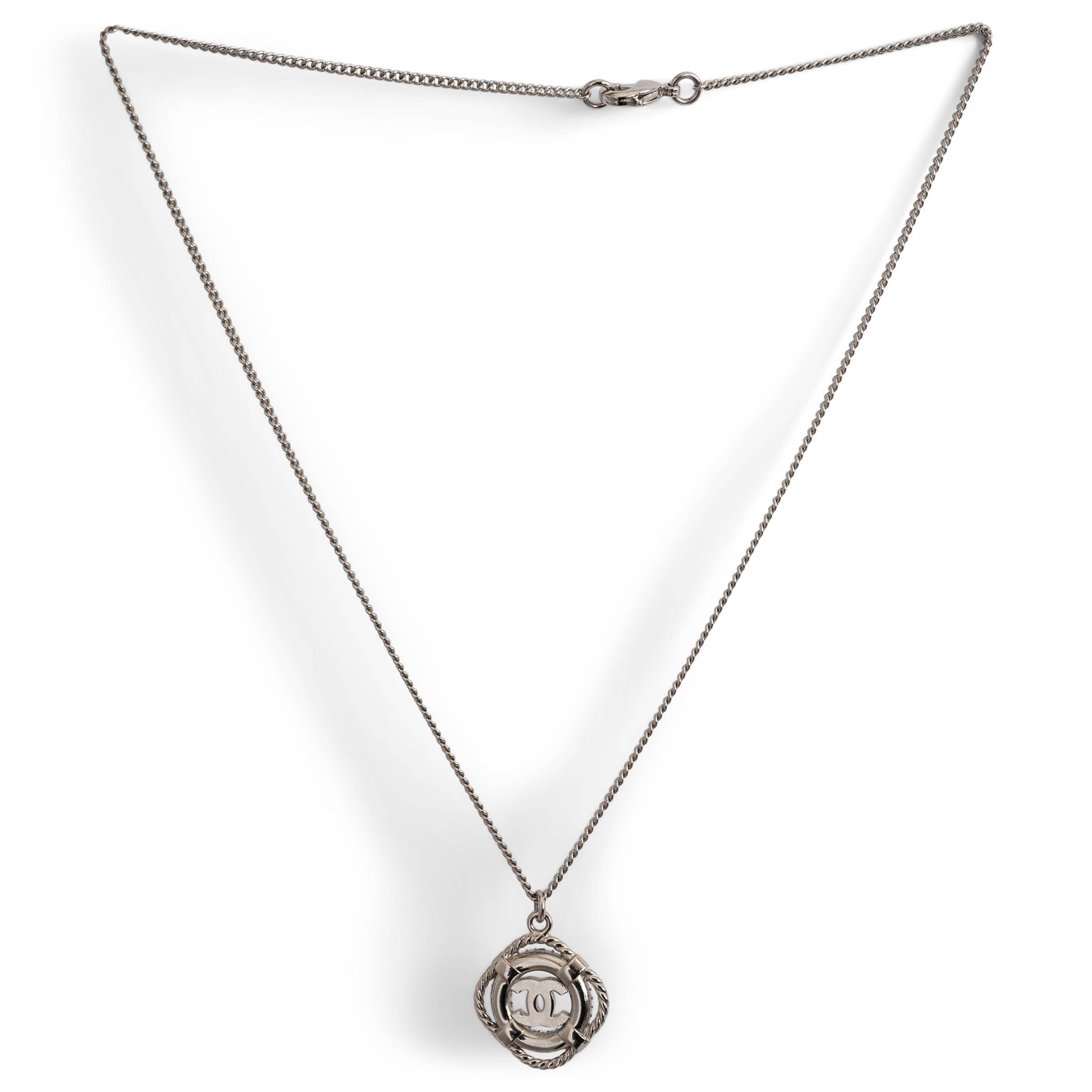 Questa collana Chanel, autentica al 100%, presenta una delicata catena in tonalità argento con un ciondolo salvagente tempestato di cristalli trasparenti, con il logo CC al centro. Un pezzo raffinato e di grande effetto che incarna l'eleganza senza
