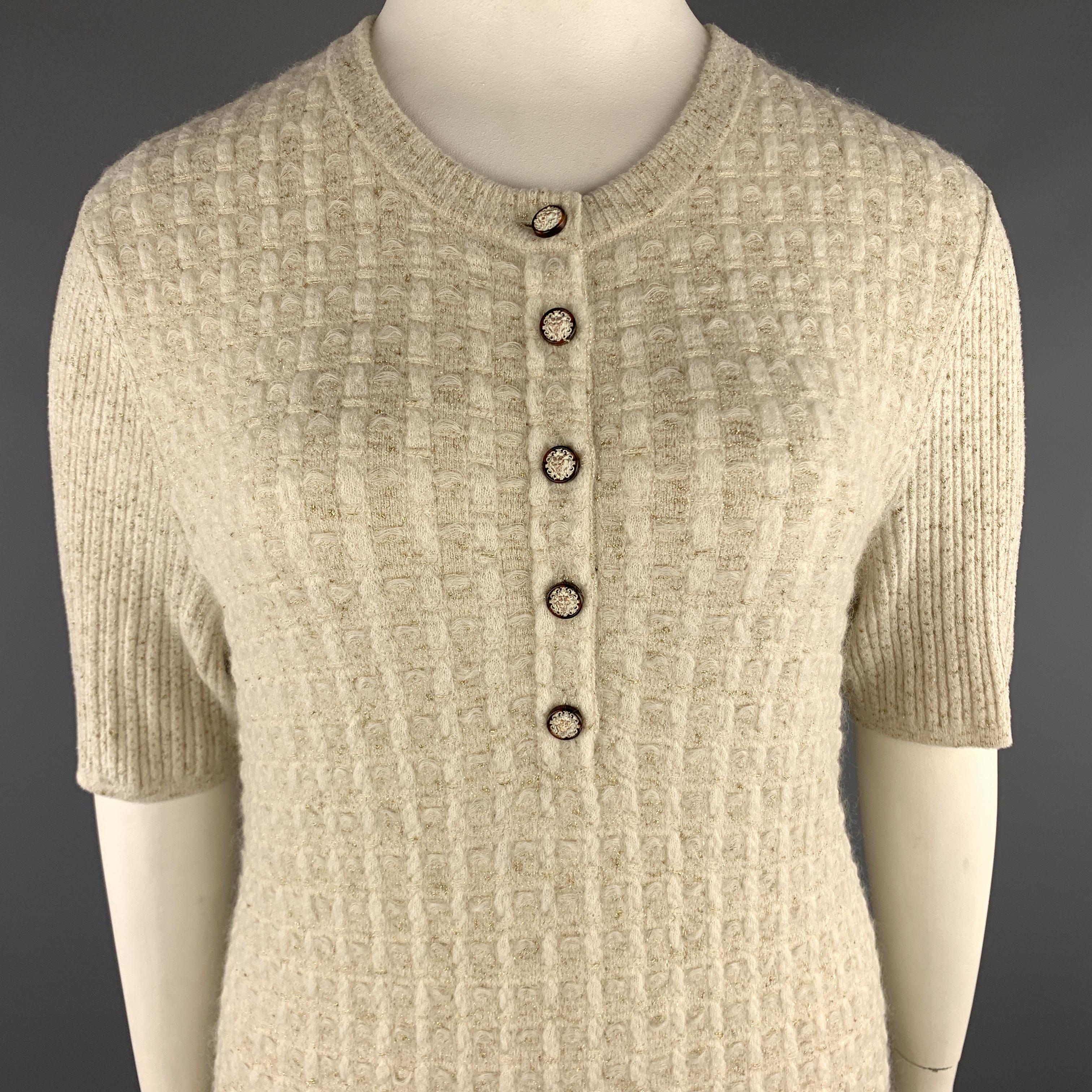 CHANEL sweater dress comes in cream tweed textured knit with metallic gold sparkle texture throughout and features a scoop neck with henley lion head button closure, short ribbed sleeves, and A line silhouette with patch pockets. Made in