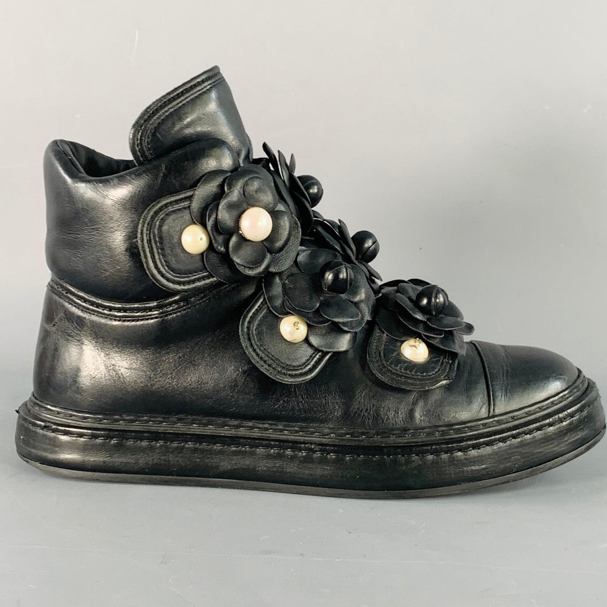 CHANEL Turnschuhe
aus schwarzem Leder mit Kamelienblüten-Applikationen aus schwarzem Leder, weißem Perlenimitat am Riemen und Schnappverschluss. Mäßige Gebrauchsspuren. 

Markiert:   L G31628 37Außensohle: 10 Zoll  x 3,75 Zoll 
  
  
 
Sui