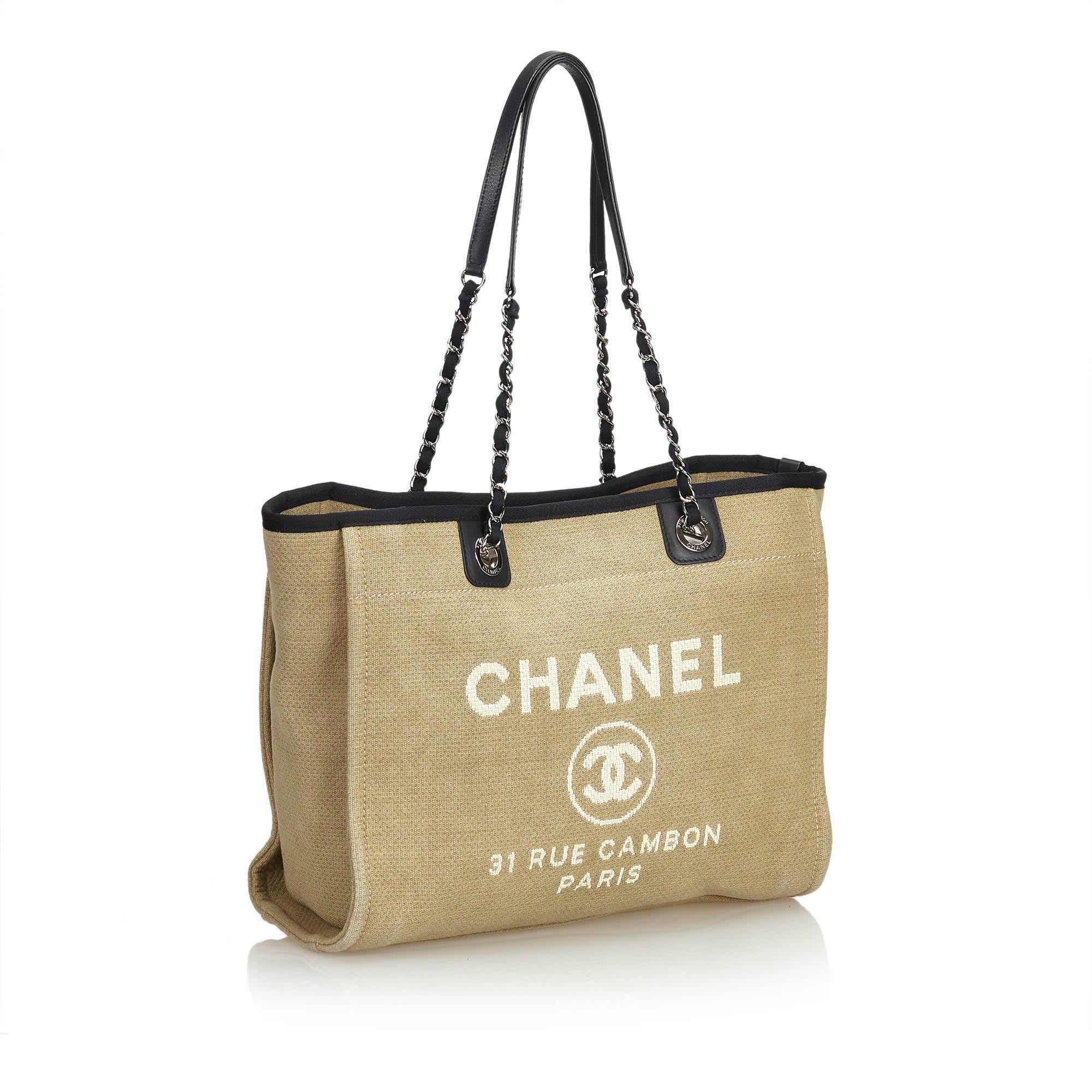 The Chanel Small Deauville logo tote bag features a canvas body, rolled black leather handle with silver-tone chain, an open top, and an interior zip and slip pocket. Comes with dust bag. 

Serial number: 16088717
Strap drop: 25cm
