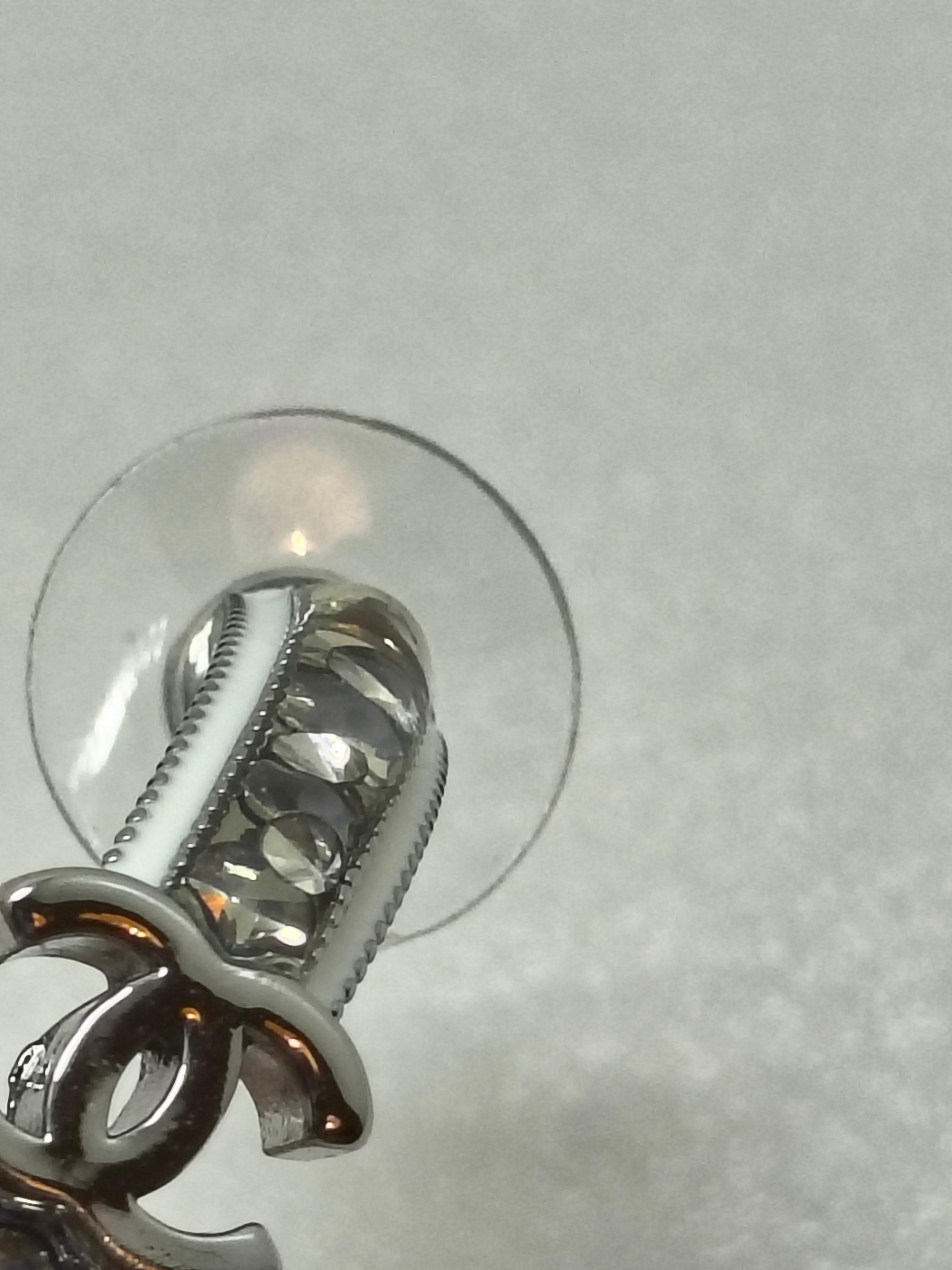 Pendientes Chanel de aro pequeño con estrás y esmalte blanco - Colección B25

Añade un sutil toque de brillo con estos elegantes pendientes de aro pequeños Chanel de la colección B25. Fabricados en un elegante metal plateado, cada pendiente presenta