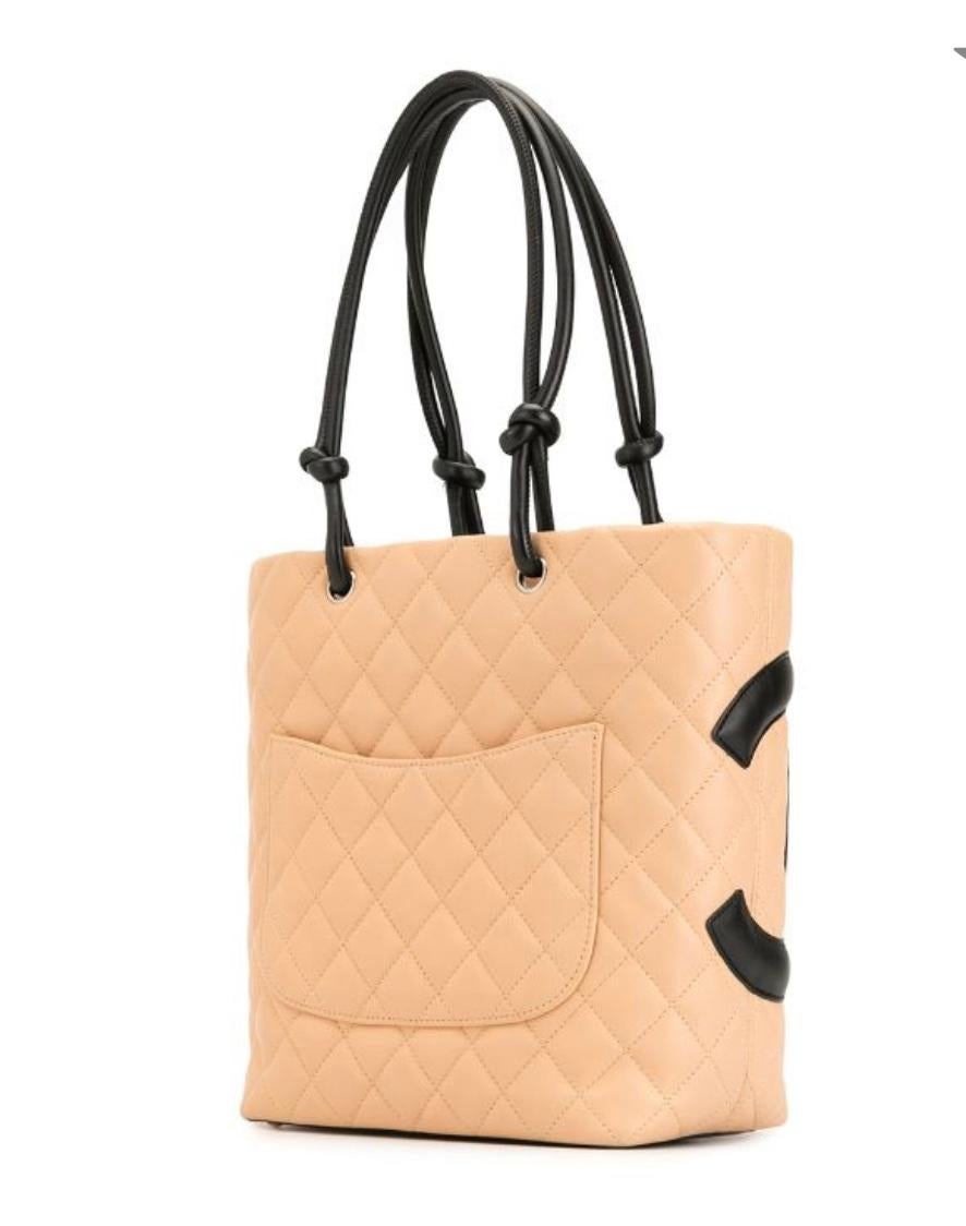 Beige quilted calfskin Chanel Ligne Cambon tote with ruthenium hardware, black leather trim, dual rolled shoulder straps, stitched CC logo appliqué at front, exterior patch pocket at back, protective feet at base, black jacquard logo lining, dual