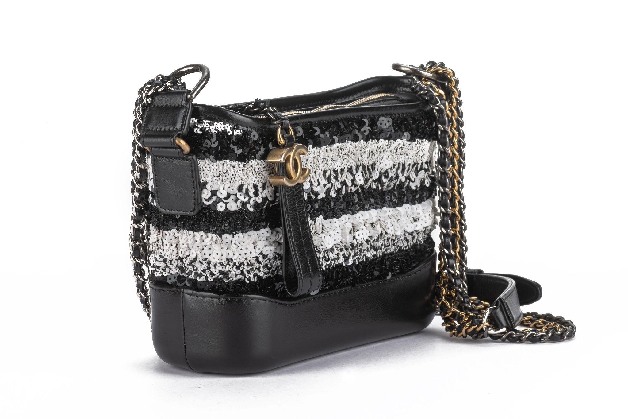 The Chanel Black and White Sequin Gabrielle Hobo from the 2019 Collection by Karl Lagerfeld features an inter-locking CC Logo on a zipper pull, chain-link adjustable shoulder strap, leather trim embellishment, canvas lining, and three interior