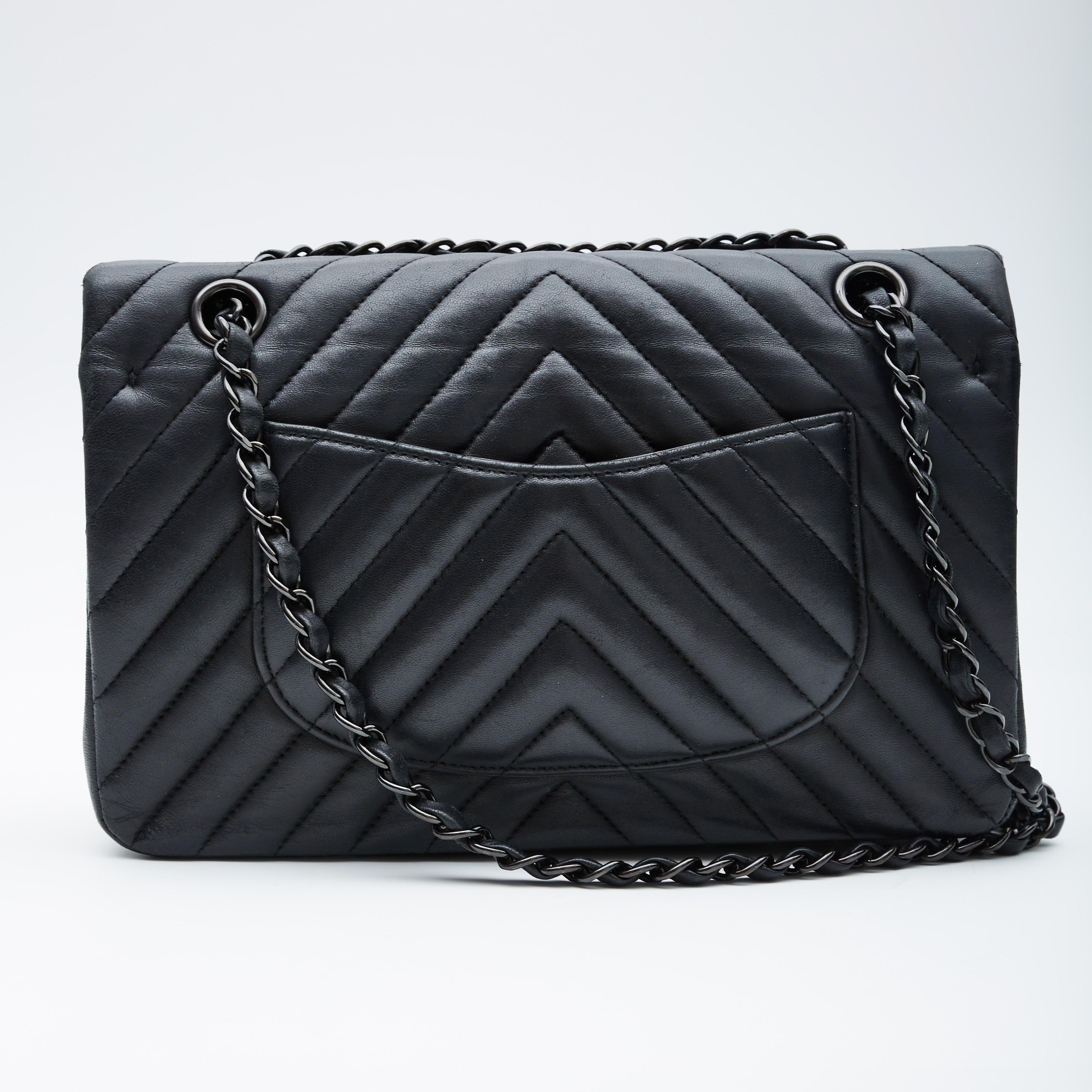 This shoulder bag is made of chevron-quilted luxurious lambskin leather in black. The bag features black chain links interlaced with leather shoulder straps, a front flap with a black Mademoiselle Chanel CC turn lock, a second flap with snap closure
