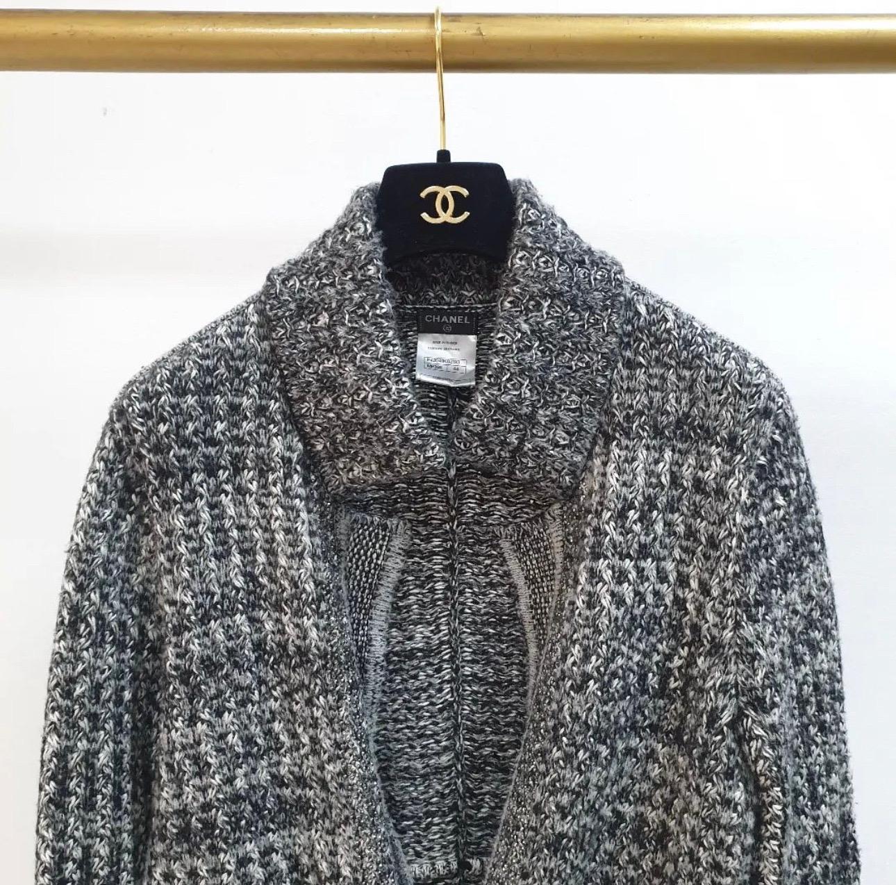 Magnifique veste en cachemire gris, noir et blanc, fermée par une chaîne argentée avec le logo Chanel.
cachemire (38%), soie (38%), laine (17%) et nylon (7%). 
Deux poches ouvertes sur le devant. 
Se noue avec de la dentelle sur le devant.