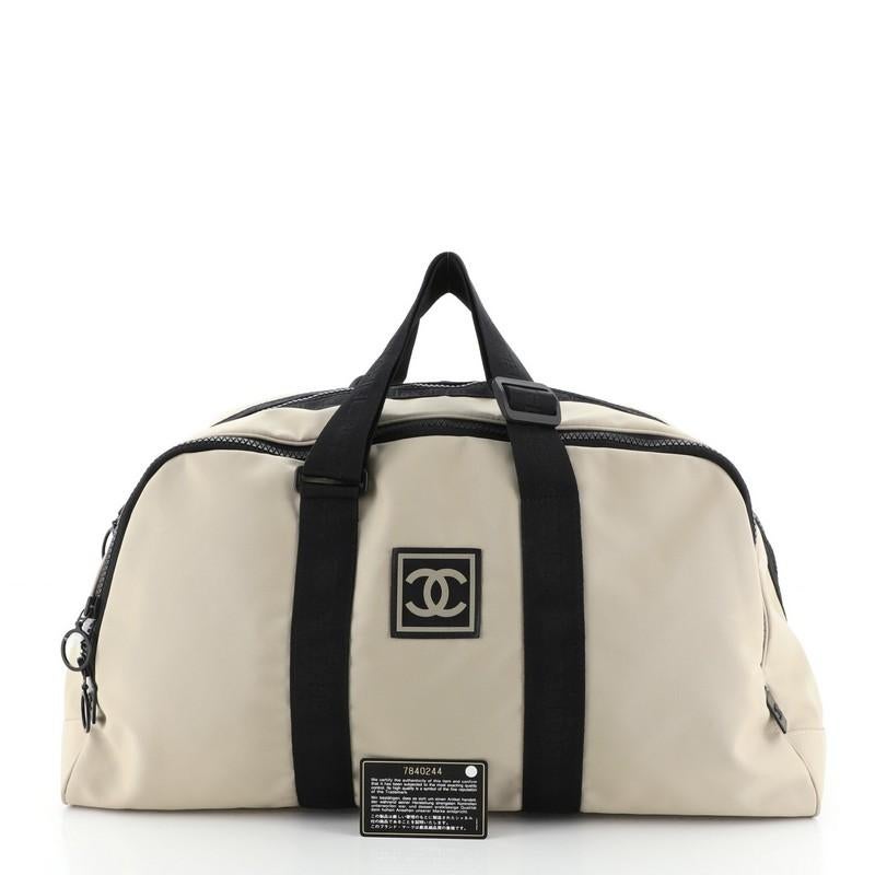 This Chanel Sport Line Duffle Bag Nylon XL, crafted from black and neutral nylon, features interlocking CC logo at front, adjustable textile straps, exterior zip compartment, and black-tone hardware. Its zip closure opens to a black fabric interior.