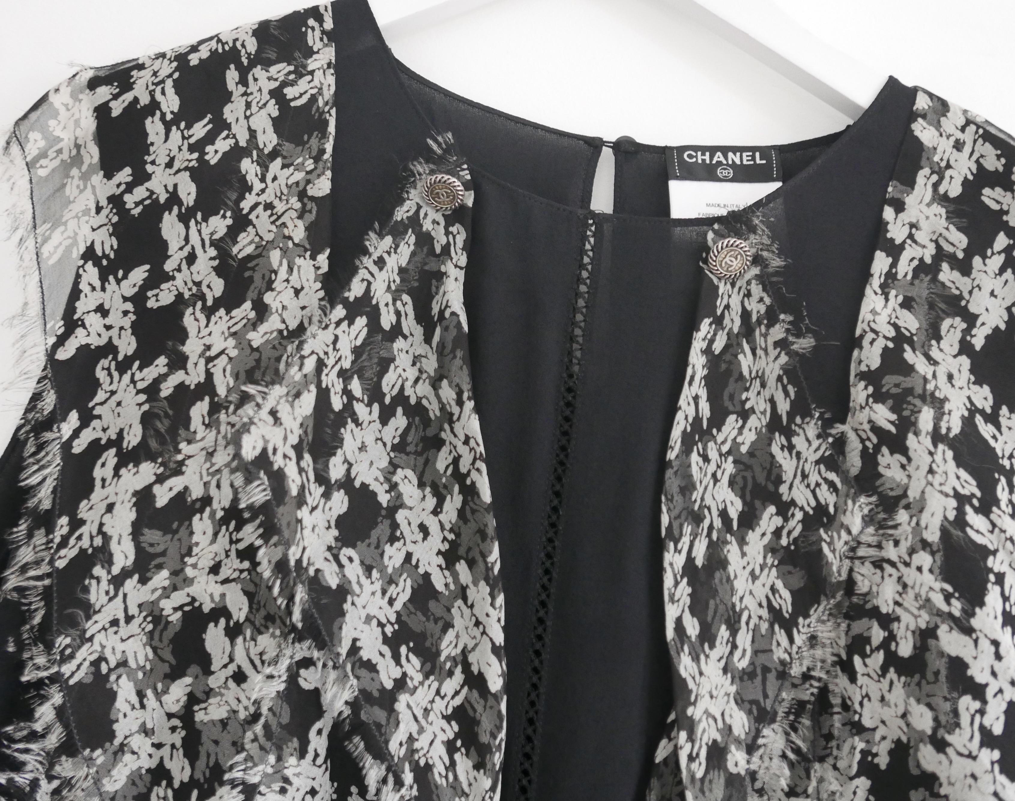 Gorgeous Chanel blouse from the Spring 2010 Collection. Unworn.
Made from matte black silk with frothy, raw edged houndstooth print silk ruffles to the front. It has thin ladder weave detail to centre front, silvertone metal and clear resin CC