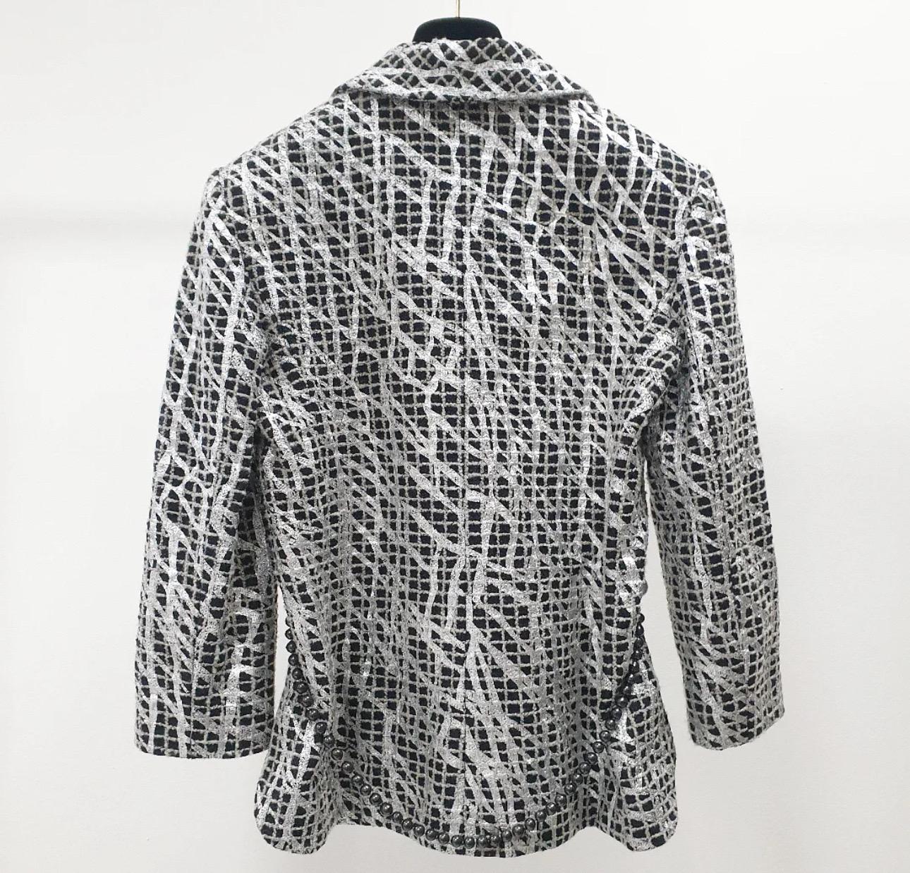 Questa giacca doppiopetto Chanel è un pezzo unico della Collection'S 2012. 

Il tweed a quadri bianchi e neri è impreziosito da vernice metallizzata argento in stile graffiti. Presenta una chiusura sicura con bottoni argentati a mezza sfera,
