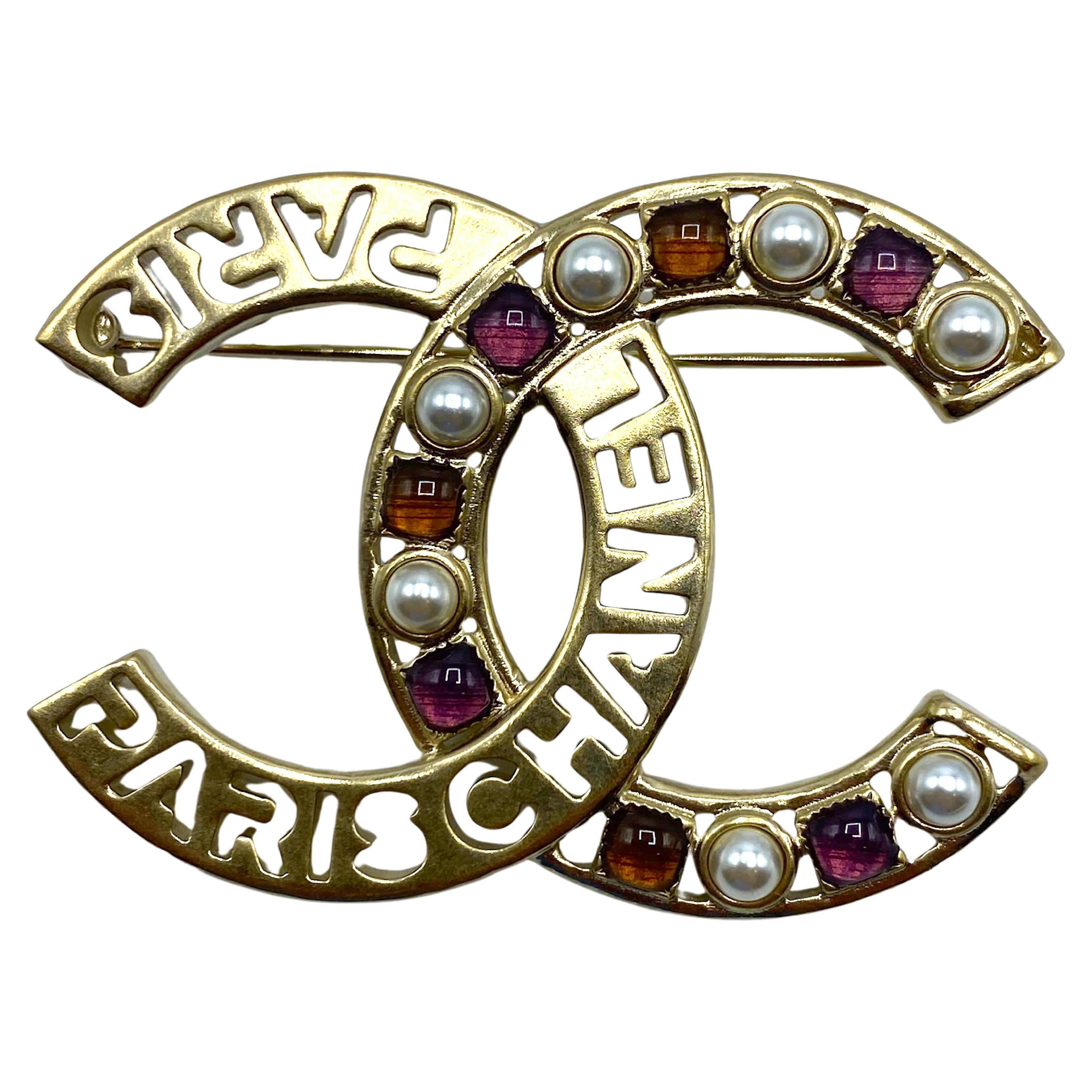 Chanel ikonische ineinandergreifende CC-Logo-Pin aus der Frühjahrskollektion 2020. Das Design zeigt auf dem linken C den Namen Chanel und zwei Ausschnitte der Heimatstadt Paris. Das rechte C ist mit Kunstperlen und Gripoix-Glassteinen in Honiggold