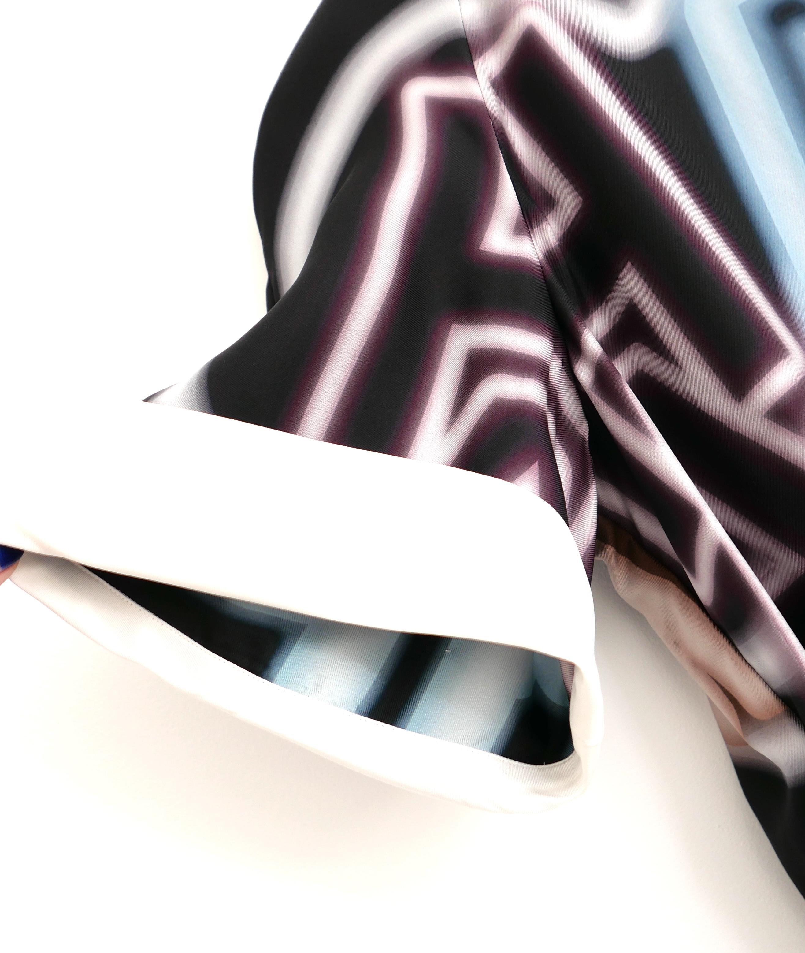 Superbe blouse à imprimé néon de Chanel, issue de la collection printemps 2021. Porté une fois. Fabriqué en soie lisse et imprimé d'un logo néon multicolore. Il présente une coupe ample, des manches courtes à revers et des boutons CC en résine et en