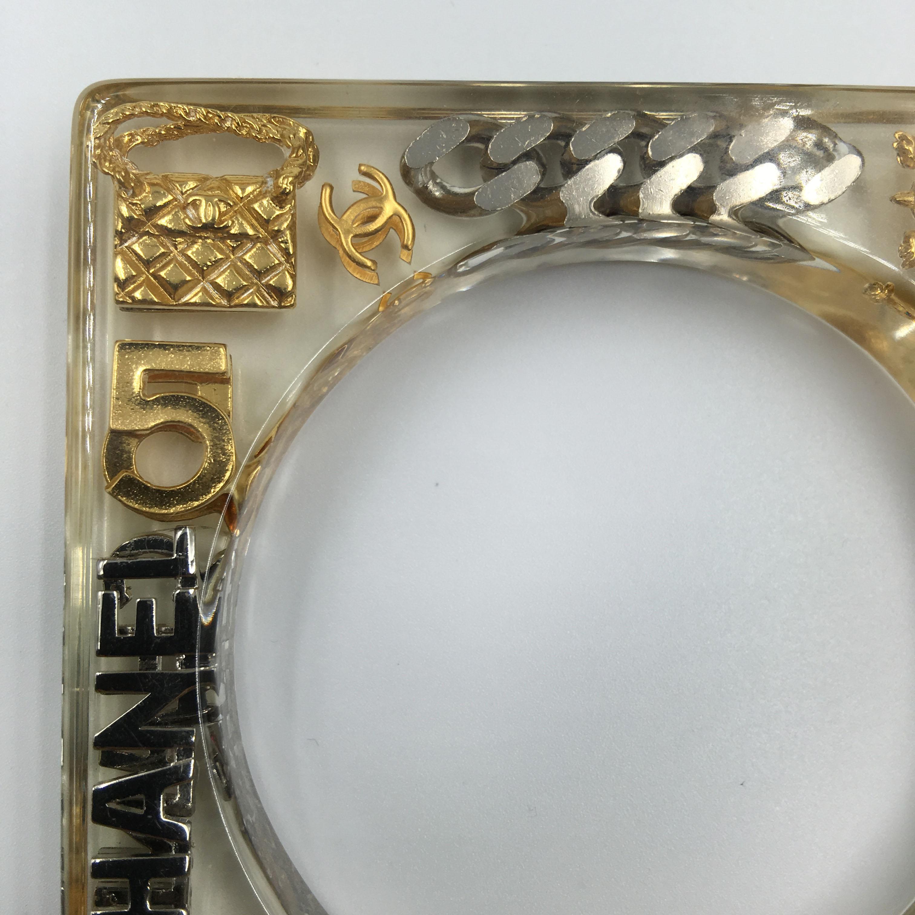 Chanel Square Lucite Bangle with Classic Chanel Gold and Silver Inlaid Charms. No scratches and lucite is clear and not yellowed. Very good vintage condition. 

Measurements is as follows:

Width- 3 3/8