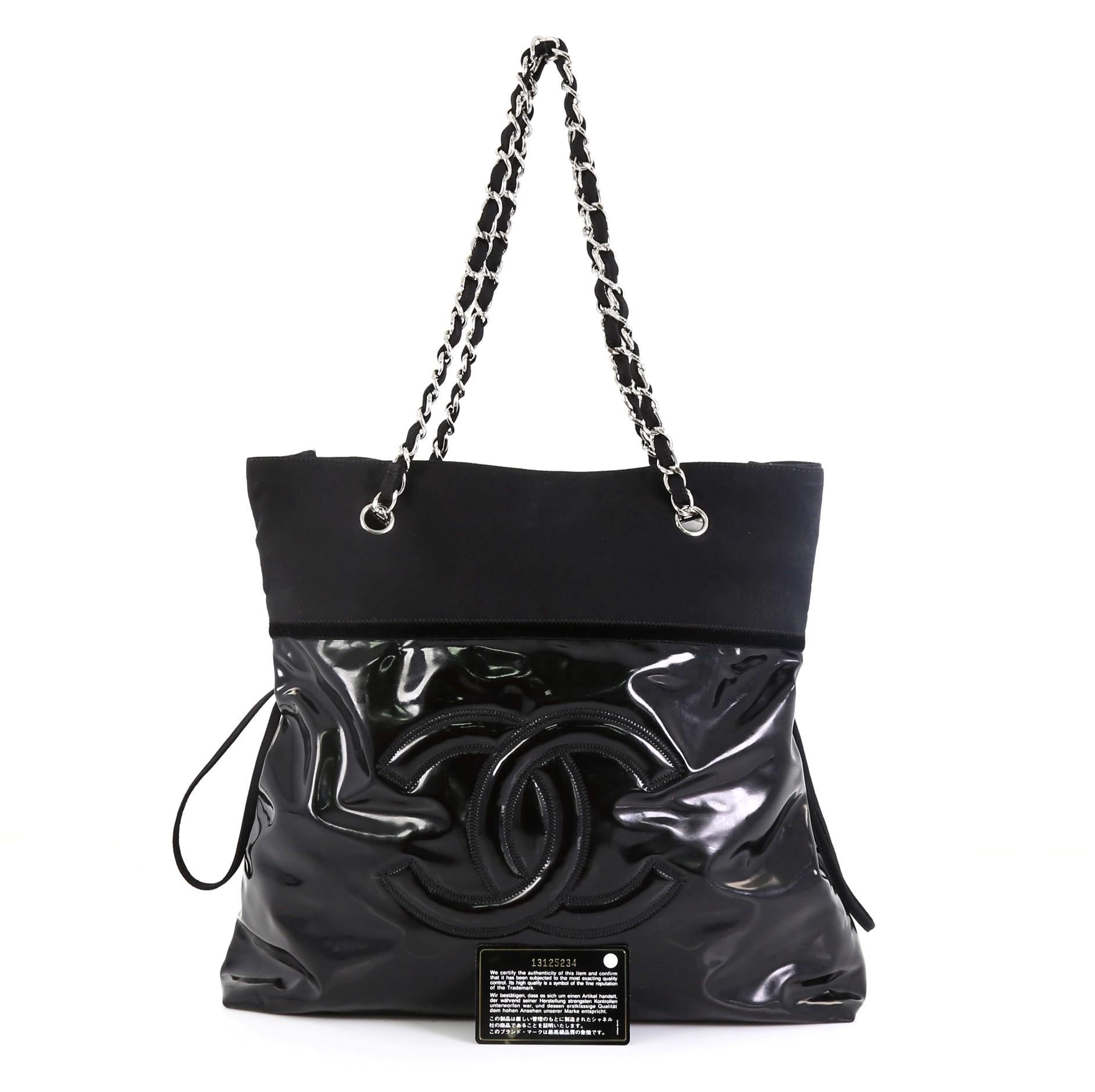 This Chanel Stretch Spirit Drawstring Tote Patent Vinyl, crafted from black patent vinyl, features woven-in fabric straps, black trims, large stitched frontal Chanel CC logo, side laces that can be cinched, and silver-tone hardware. Its magnetic