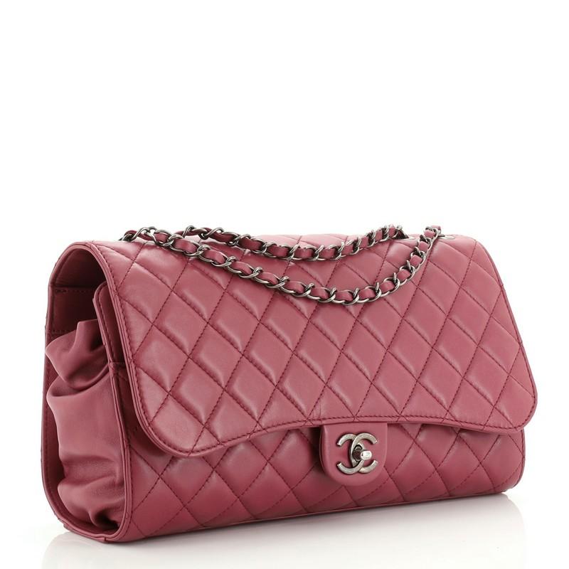 This Chanel Supermarket Drawstring Shopping Flap Bag Quilted Lambskin Jumbo, crafted from purple leather, features a woven in chain link strap, exterior back pocket, and aged silver tone hardware. Its flap closure opens to a purple satin drawstring