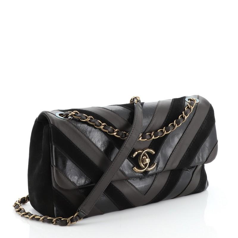 This Chanel Surpique CC Flap Bag Chevron Lambskin and Suede Jumbo, crafted from black and brown chevron lambskin leather and suede, features woven-in leather chain strap and aged gold-tone hardware. Its CC turn-lock closure opens to a red fabric