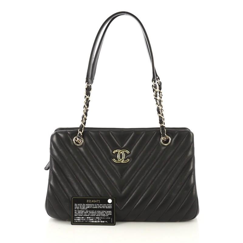 This Chanel Surpique Chain Zip Tote Chevron Lambskin Large, crafted from black chevron lambskin leather, features a woven-in leather chain straps with shoulder pads and gold-tone hardware. It opens to a burgundy leather interior with middle zip