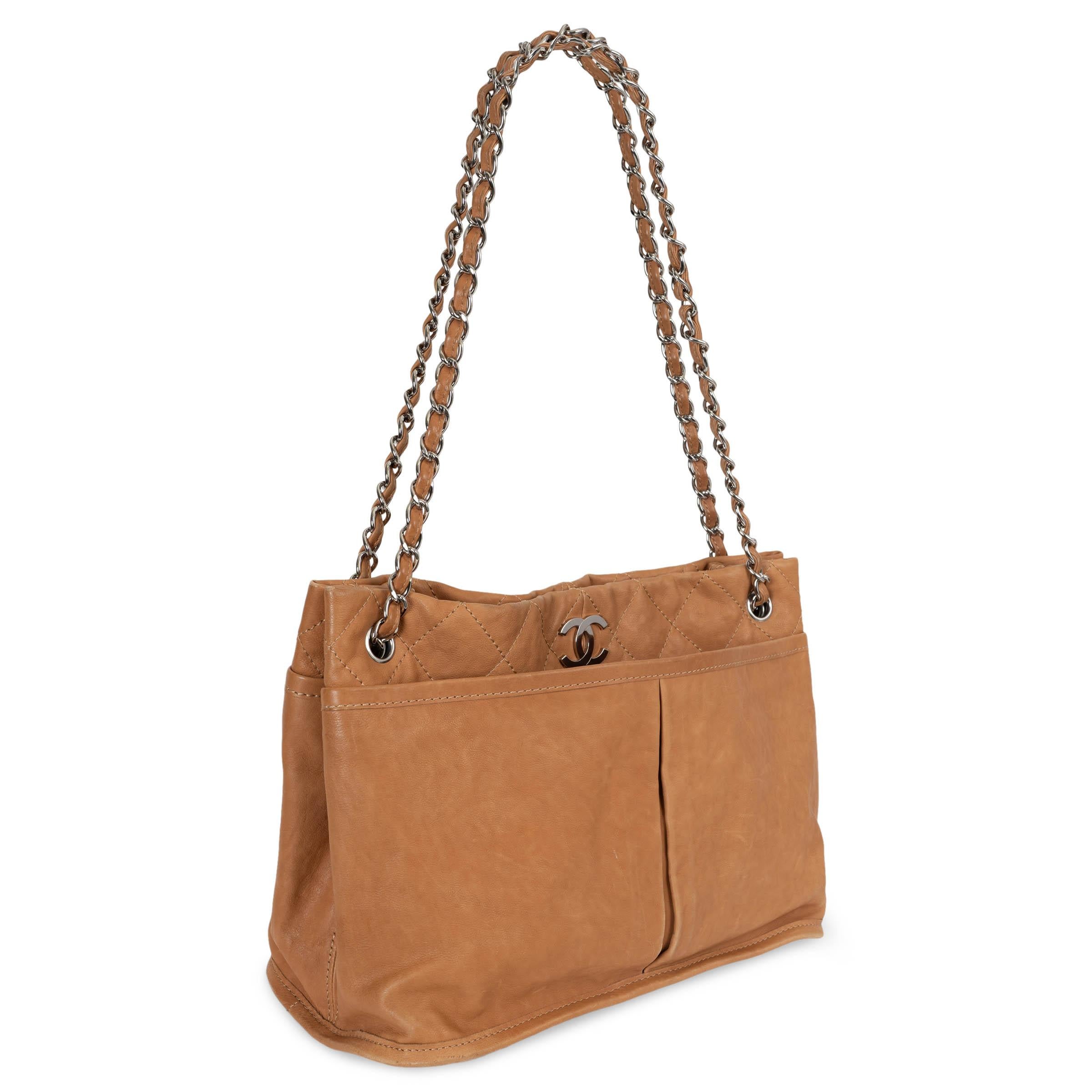 This 100% authentic Chanel light cognac calfskin leather Natural Beauty  tote bag is a perfect blend of elegance and practicality. It features a wide pleated front and rear pocket, a silver-tone chain-link shoulder strap threaded with leather, and a