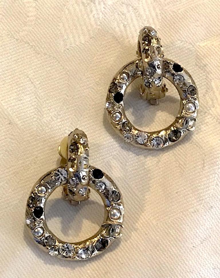 An elegant pair of Chanel textured hoop dangle earrings. Each satin gold tone earring is cast in a martele' rough texture and set with clear, grey and black rhinestones and mini pearls on the front. With attention to detail, Chanel set the  back of