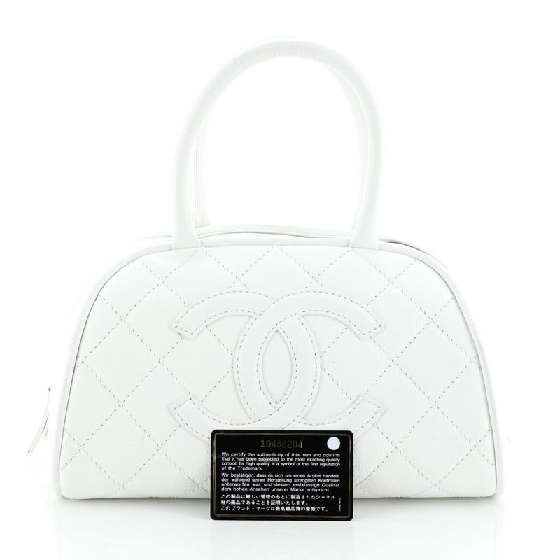 This Chanel Timeless CC Bowler Bag Quilted Caviar Mini, crafted in white quilted leather, features dual rolled leather handles, stitched CC logo across the front, and aged silver-tone hardware. Its top zip closure opens to a white fabric interior