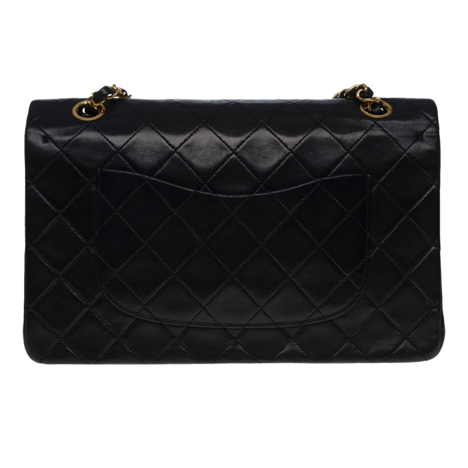 El codiciadísimo bolso Chanel Timeless mediano de 25 cm con doble solapa de piel acolchada negra, herrajes de metal dorado, una correa de cadena de metal dorado entretejida con piel negra que permite llevar el bolso al hombro o cruzado.

Bolsillo de