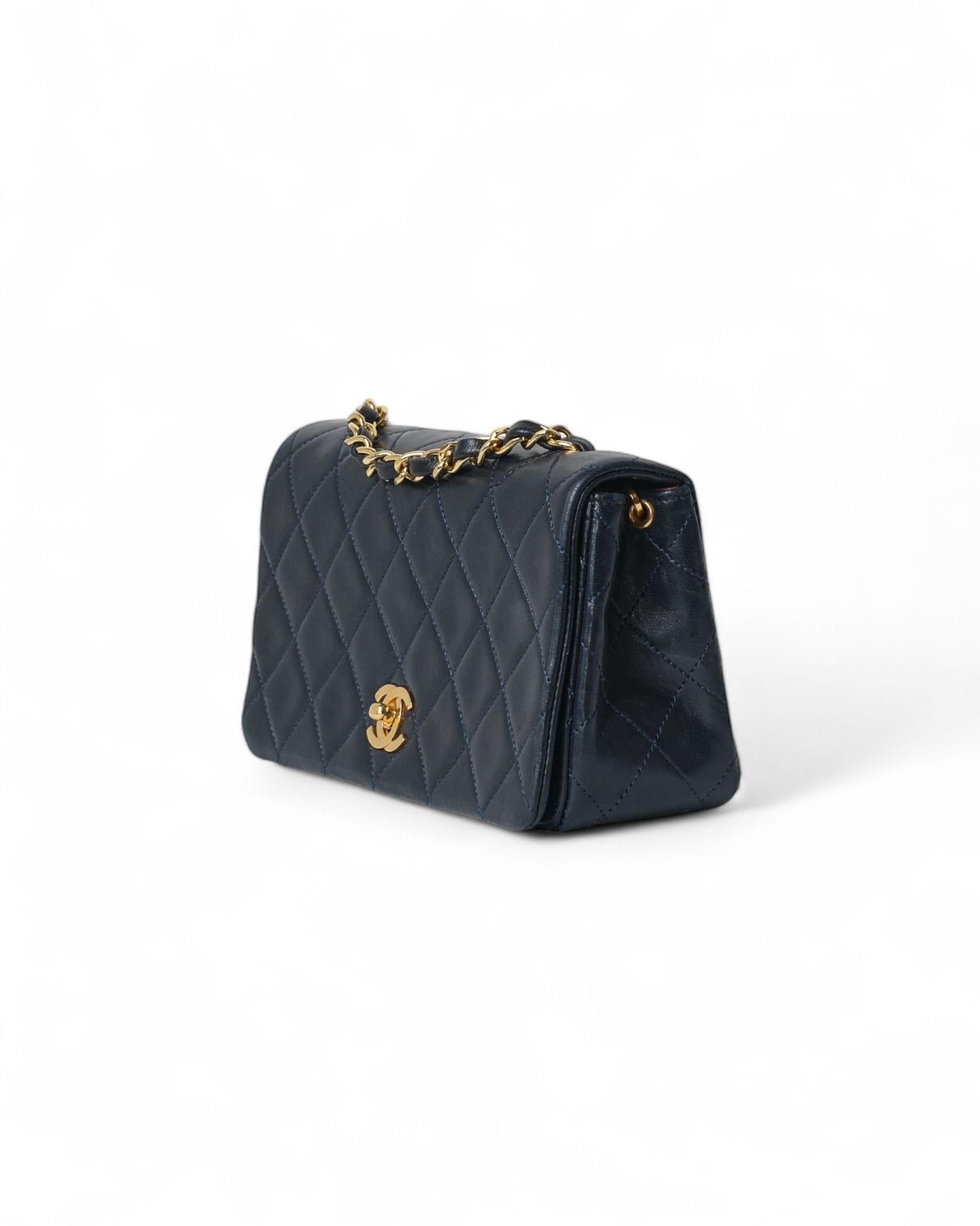 Borsa firmata Chanel, linea Timeless, modello Mini Flap vintage, realizzata in pelle liscia di alta qualità nella raffinata tonalità blu, con l’iconico hardware dorato che aggiunge un tocco di lusso discreto. La patta frontale si chiude con il