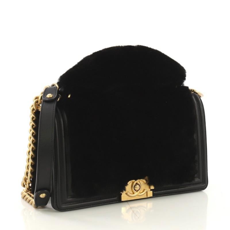 This Chanel Top Handle Boy Flap Bag Fur Old Medium, crafted from black fur and leather, features a chain link strap with shoulder pad, top handle, and aged gold-tone hardware. Its CC boy push-lock closure opens to a black leather interior with a