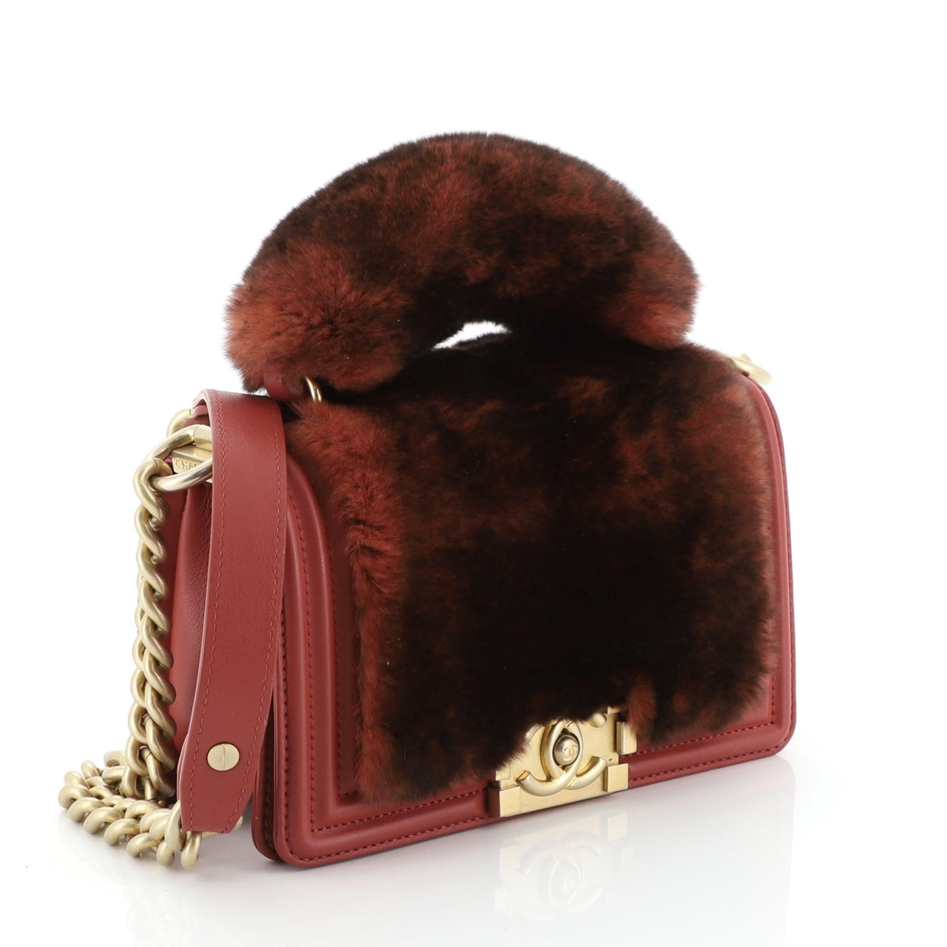 This Chanel Top Handle Boy Flap Bag Fur Small, crafted from red fur, features chunky chain link strap with shoulder pad, fur top handle, and gold-tone hardware. Its CC boy push-lock closure opens to a red fabric interior with side slip pocket.