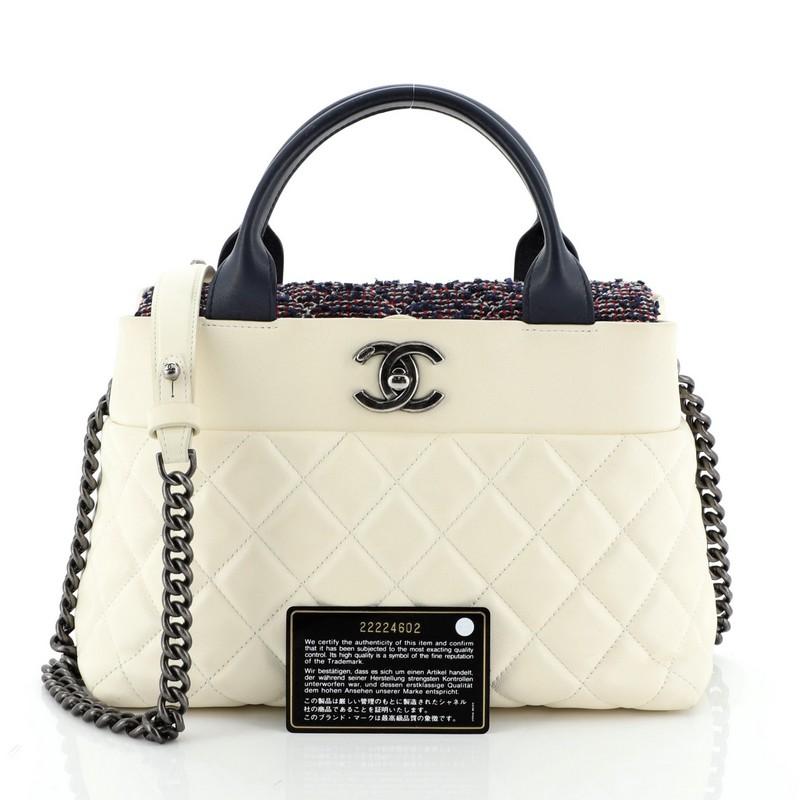This Chanel Top Handle CC Tote Quilted Calfskin with Tweed Small, crafted from blue calfskin leather and white textile, features dual rolled handles, CC logo on front, chain link strap and aged silver tone hardware. It opens to a gray fabric