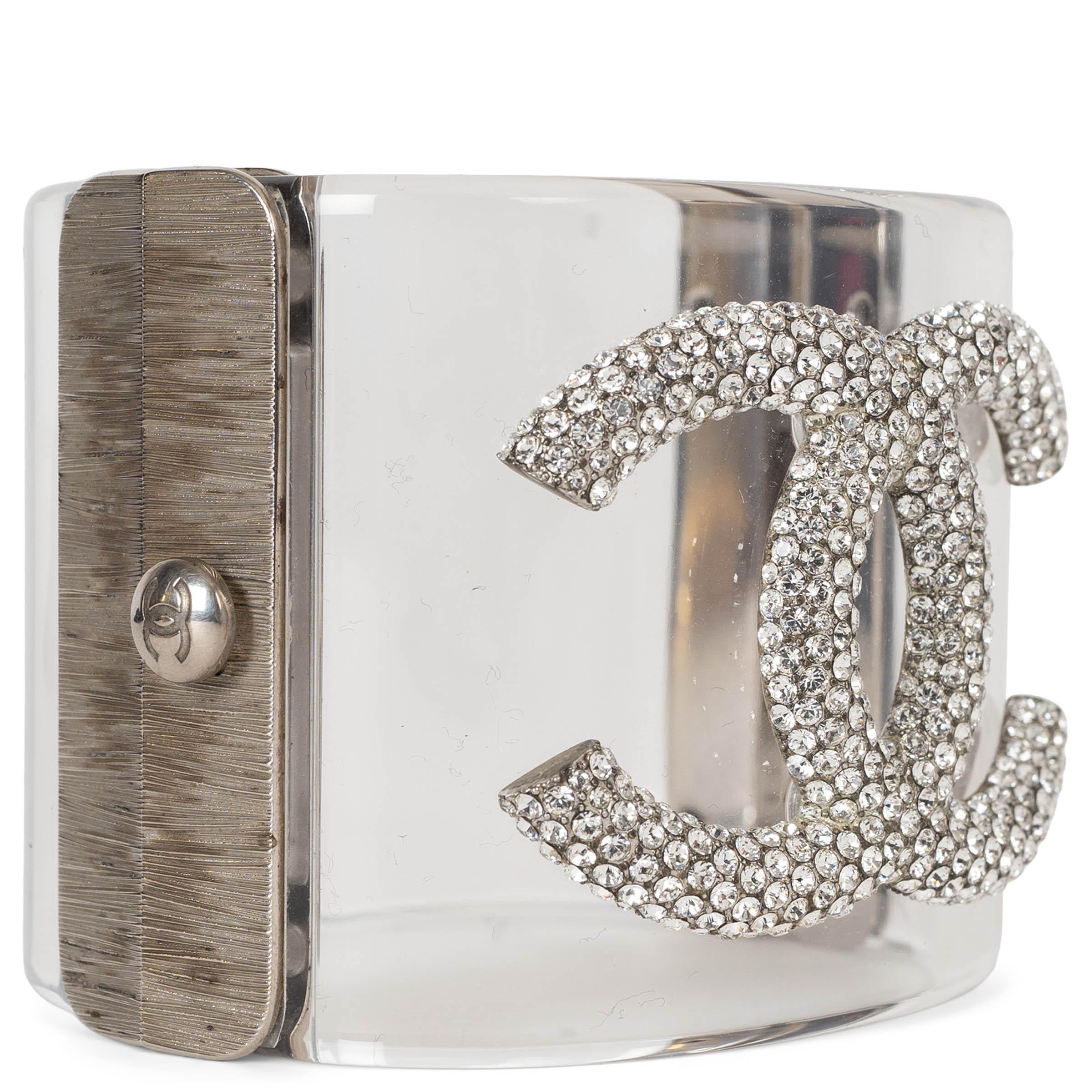 This 100% authentic Chanel cuff bracelet in clear lucite exudes modern elegance. Featuring a large crystal-adorned CC logo and silver-tone metal lock, it is a striking statement accessory that seamlessly combines contemporary design with iconic