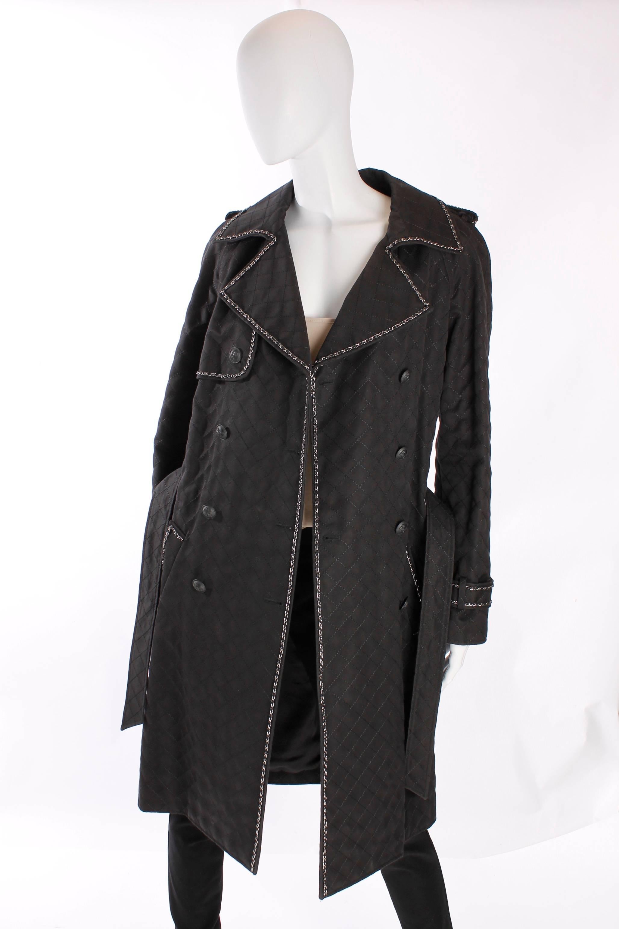 Insanely beautiful trenchcoat by Chanel, wow!!

This fully quilted coat has a large collar and lapel. Along the sides a silver chain with black leather is attached. It looks just like the shoulderstrap of the 2.55 Chanel bag! This chain is also to