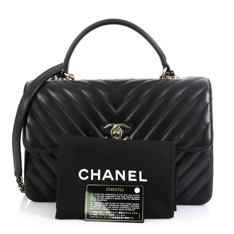 This Chanel Trendy CC Top Handle Bag Chevron Lambskin Medium, crafted from black chevron lambskin leather, features a flat leather top handle, woven-in leather chain strap with leather pad, and silver-tone hardware. Its turn-lock closure opens to a
