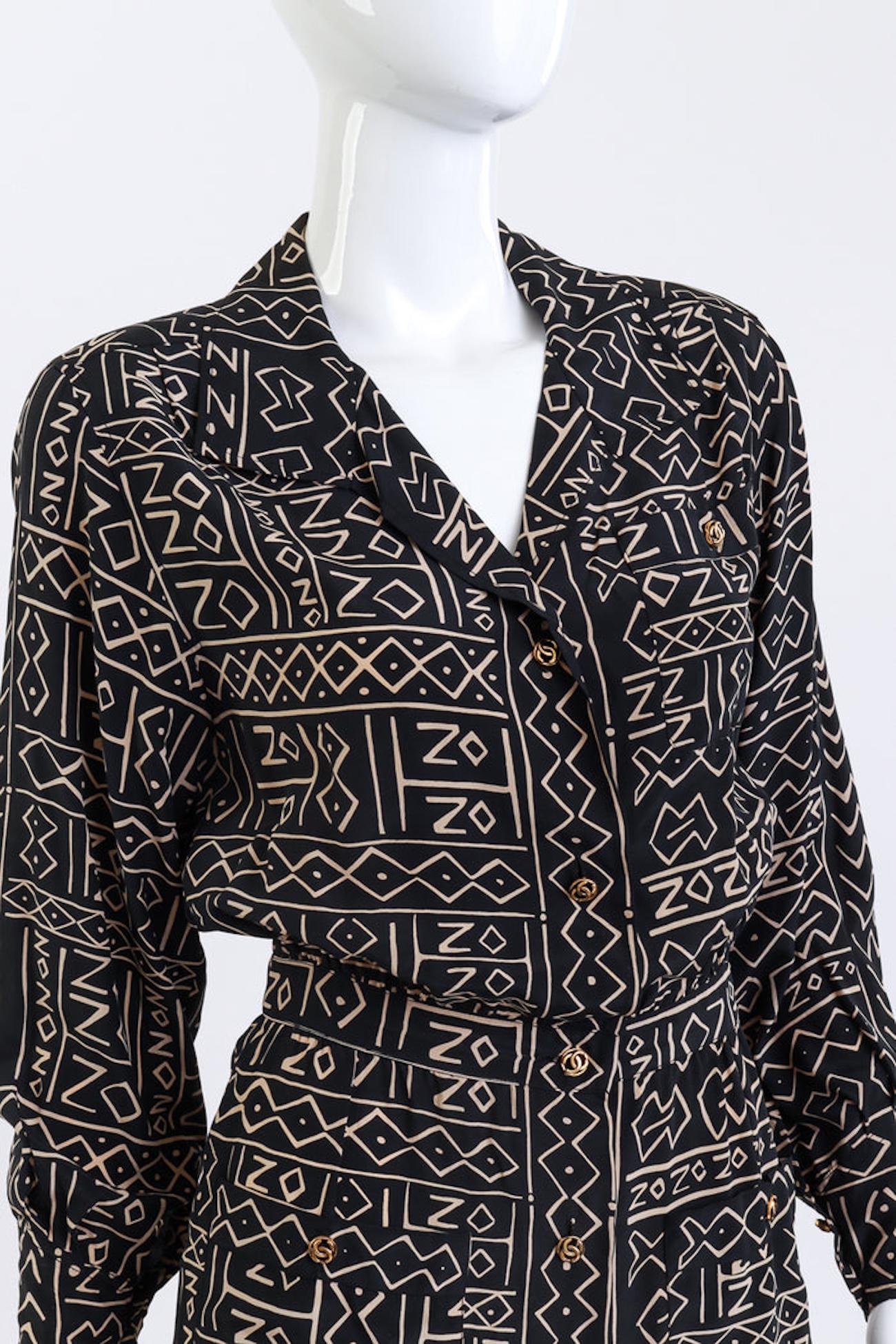 CHANEL TRIBAL PRINT SILK BUTTON-UP SHIRTDRESS (US 2-4)

This Chanel silk shirtdress features a striking tribal-inspired print in black and beige. The knee-length design includes structured shoulders, a fitted banded waist with pleated gathering, and
