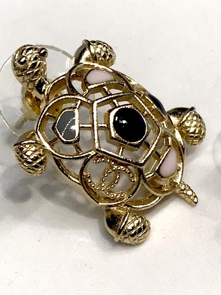 Chanel satin gold tone and enamel openwork turtle earrings with inconic Chanel interlocking CC logo from the 2019 Cruise collection. Pale pink, grey and black enamel. Small CC logo on left side above the turtle's left fin. Each earring measures .75