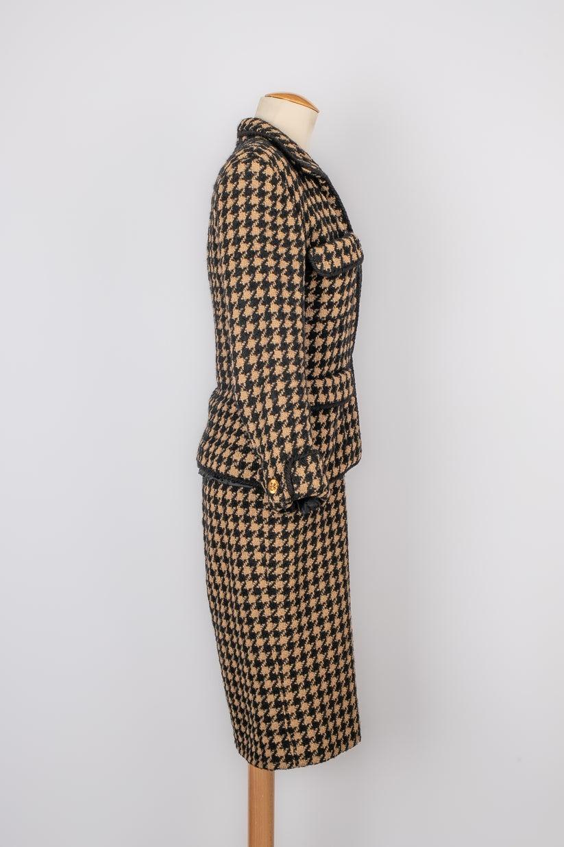 Chanel - Ensemble en tweed composé d'une veste et d'une robe à motifs pied-de-poule et boutons en métal doré représentant des trèfles à quatre feuilles. Taille 38FR indiquée.

Informations complémentaires :
Condit : Très bon état.
Dimensions : Veste